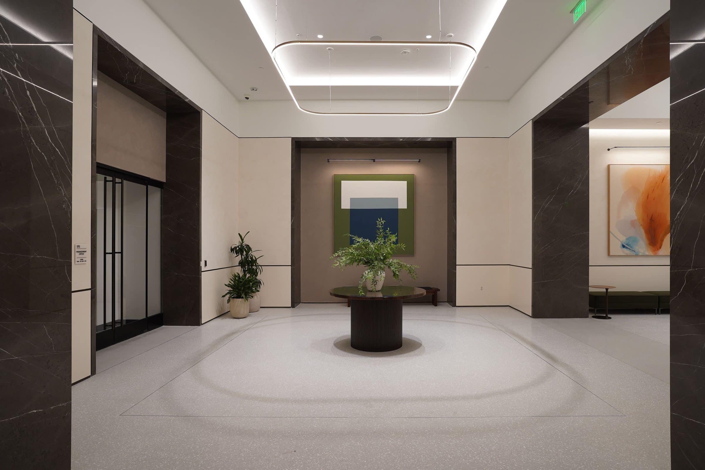 Green, blue and white geometric painting at the end of a bright lobby, with a partial orange work at right