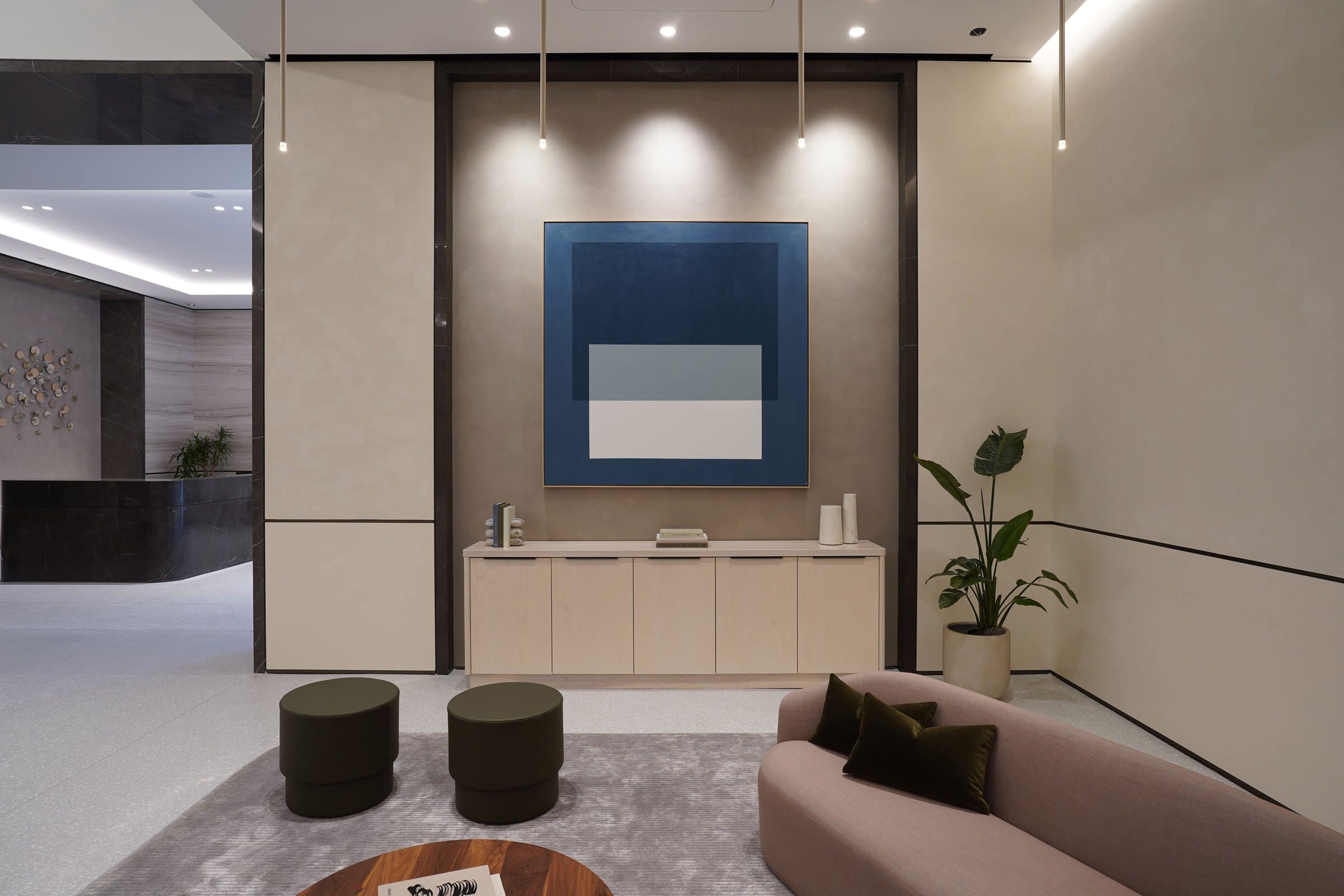 Blue and white geometric painting above a pale cabinet beside lounge seating and a potted plant