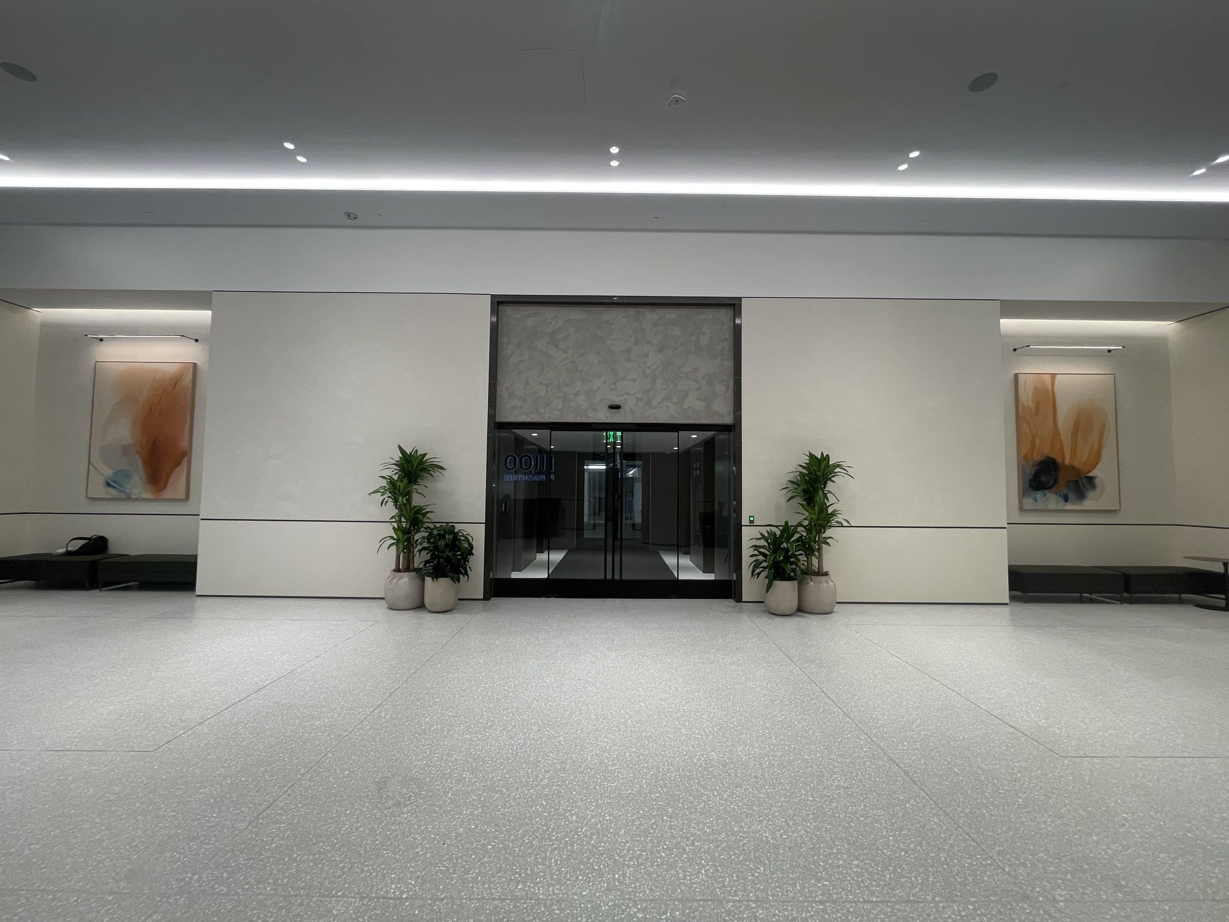 Two pale orange and blue framed paintings flank a glass entrance in a stone-floored lobby