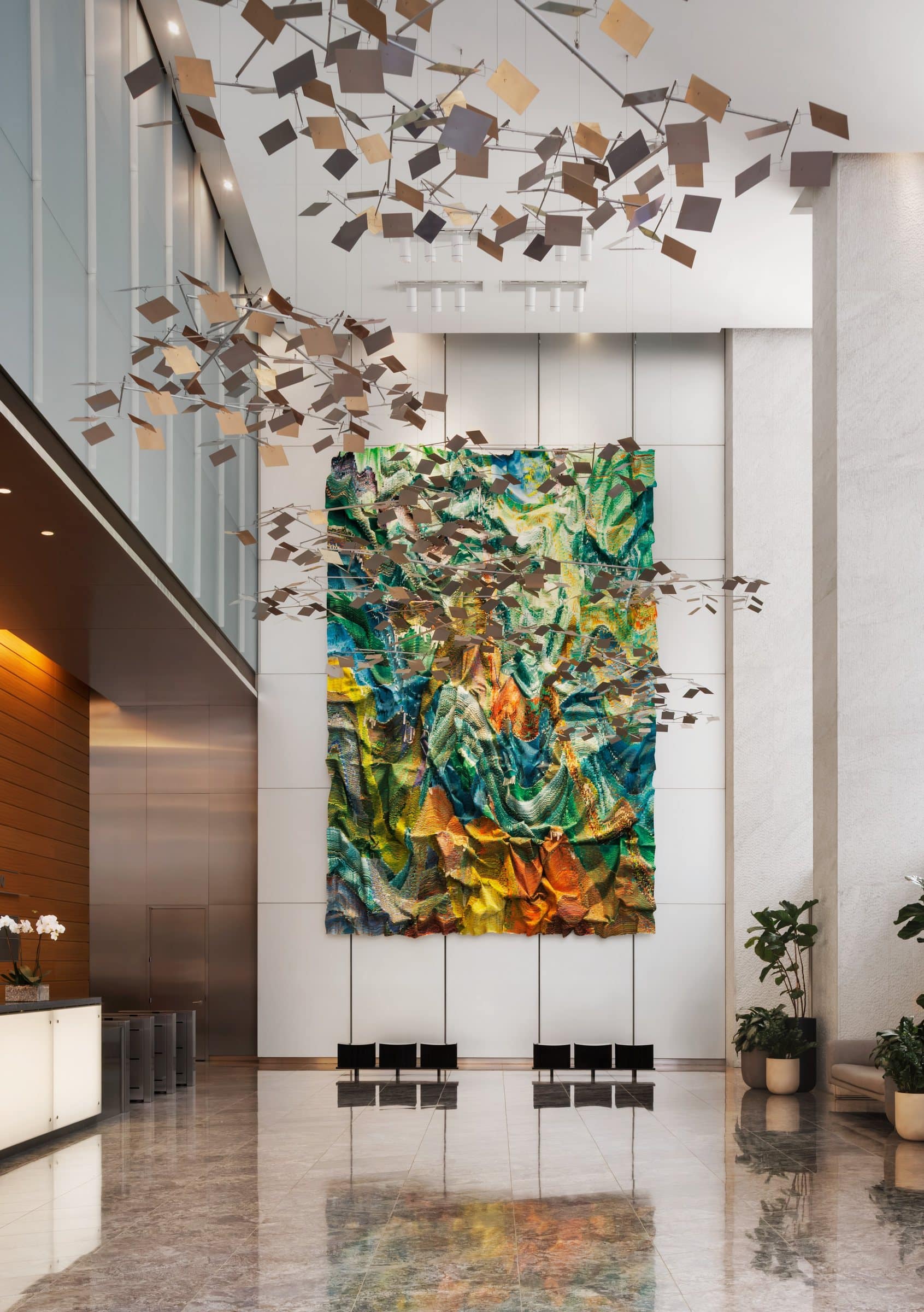 Tall green, turquoise and yellow textile work at the end of a double-height lobby beneath a suspended ceiling feature