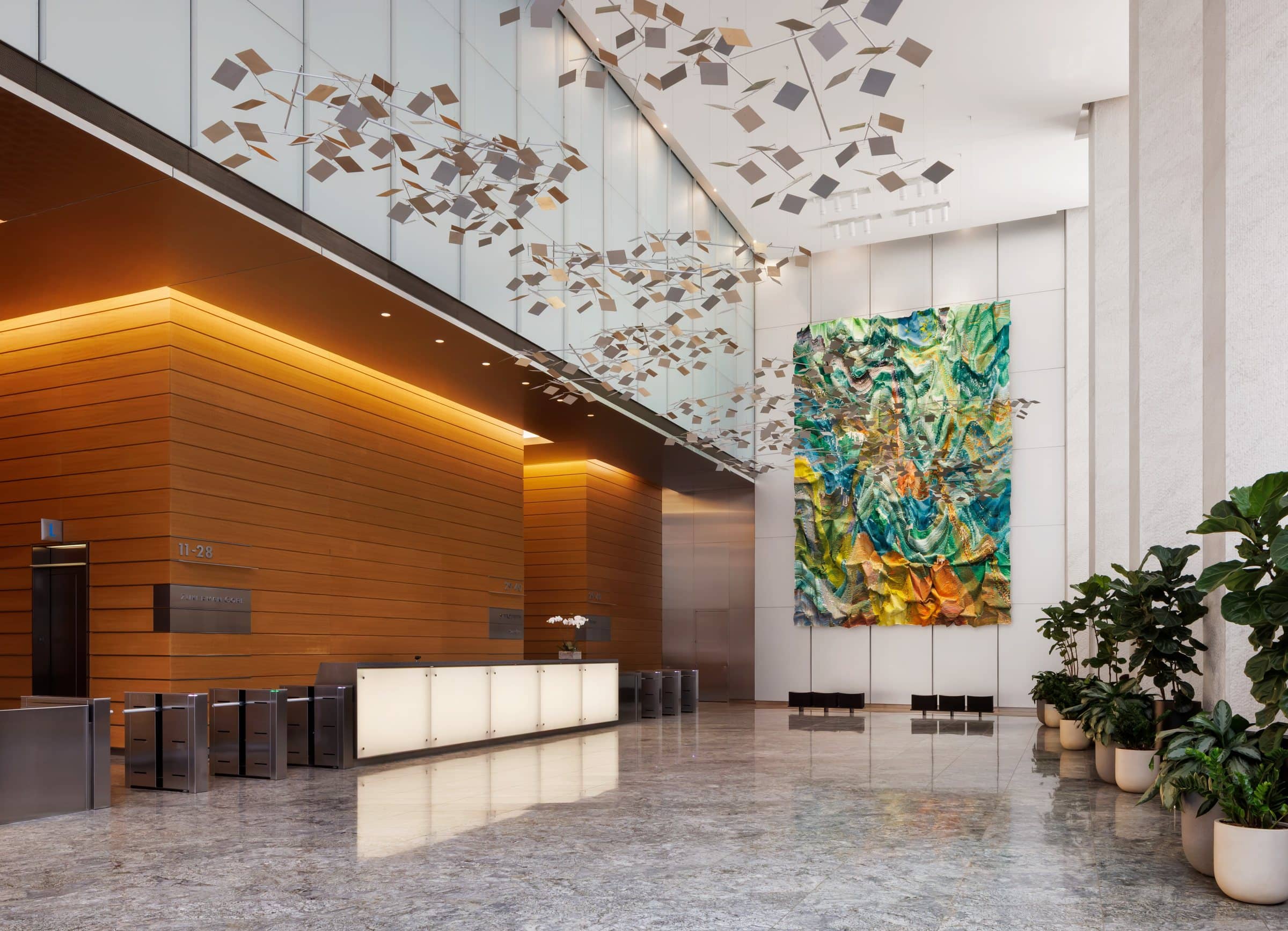 Wide stone-floored lobby with a green and yellow rippling textile work beside the wood-paneled reception area