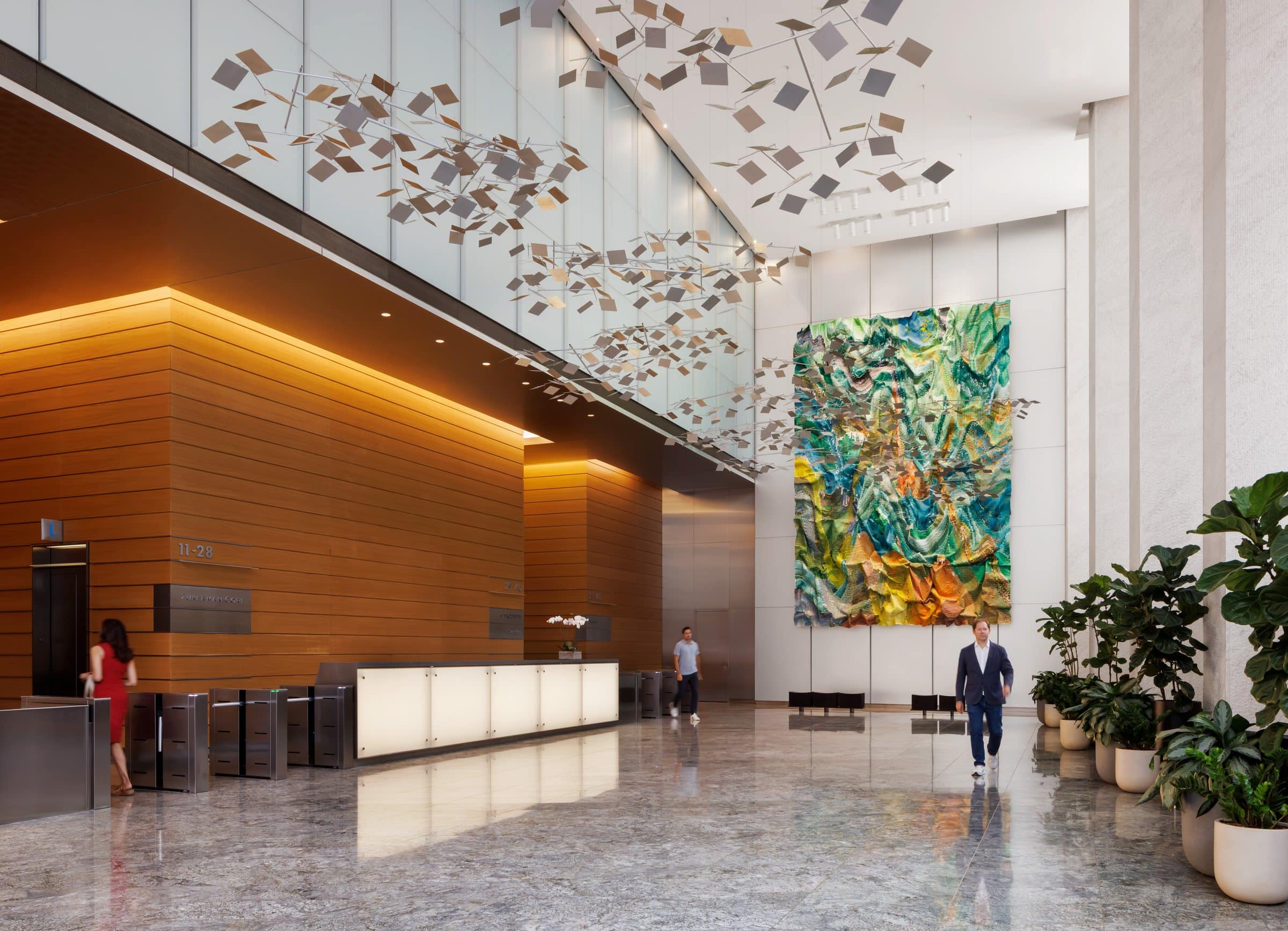 Visitors cross the lobby in front of a tall green and yellow textile work beside the reception desk