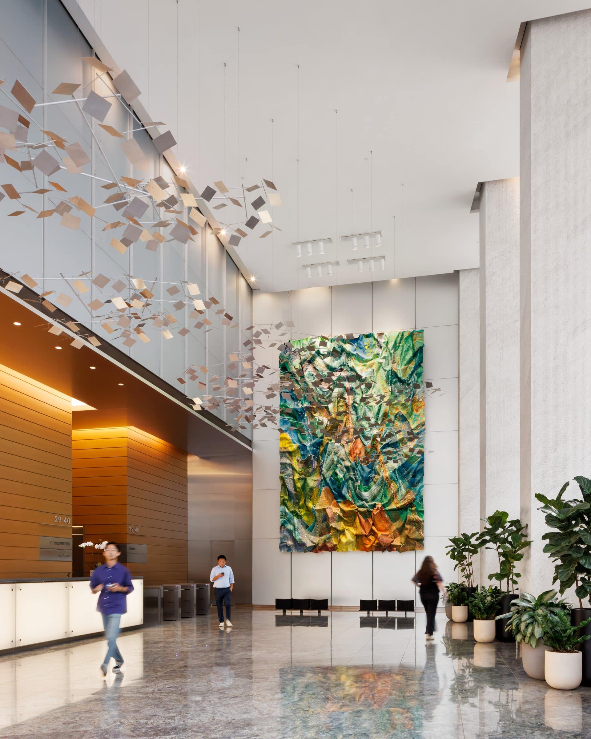 Three visitors give scale to the green and gold textile work on the far wall of the double-height lobby