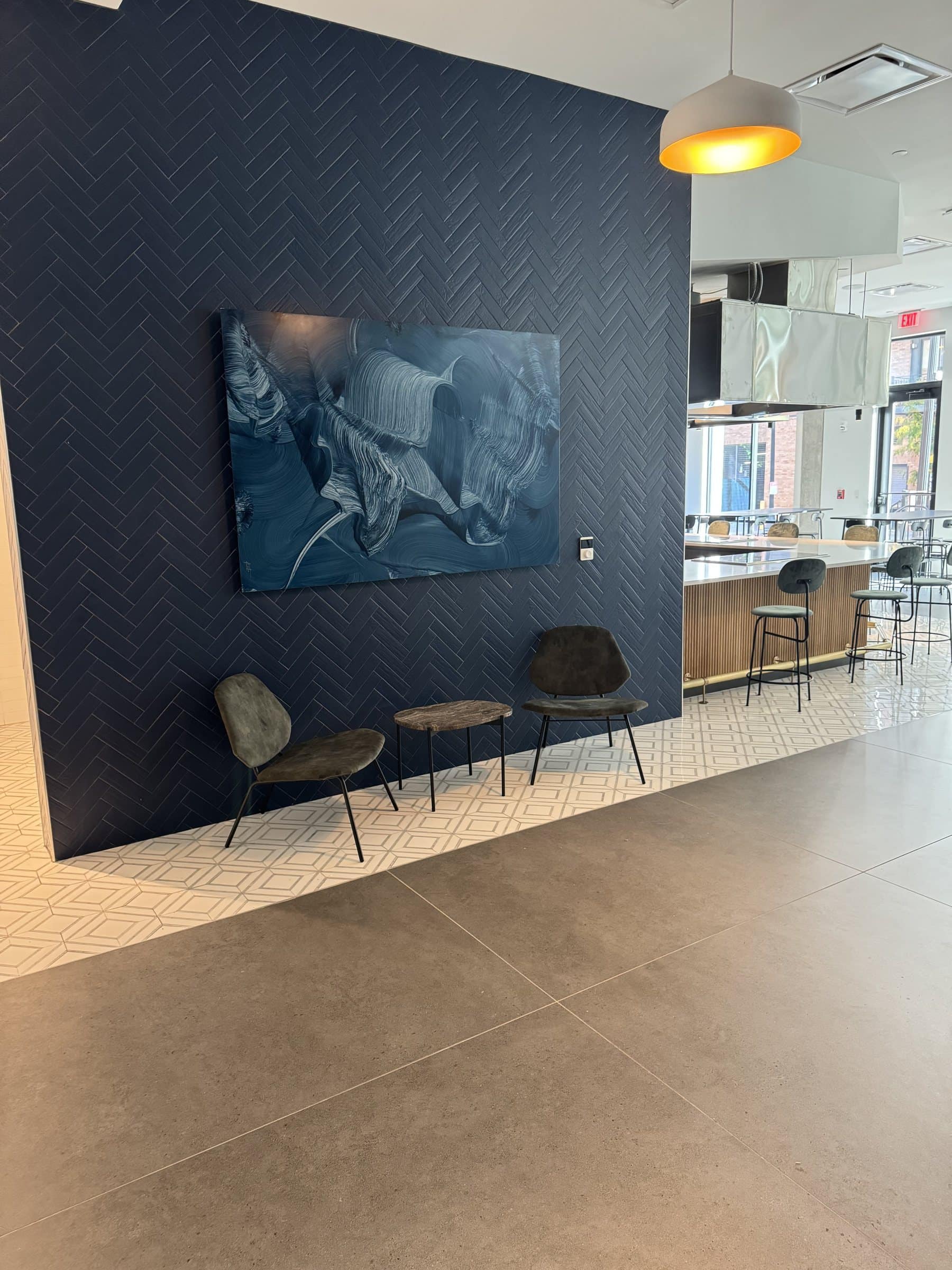 A dark gestural painting hangs above two chairs beside the shared kitchen at The Wyldes.
