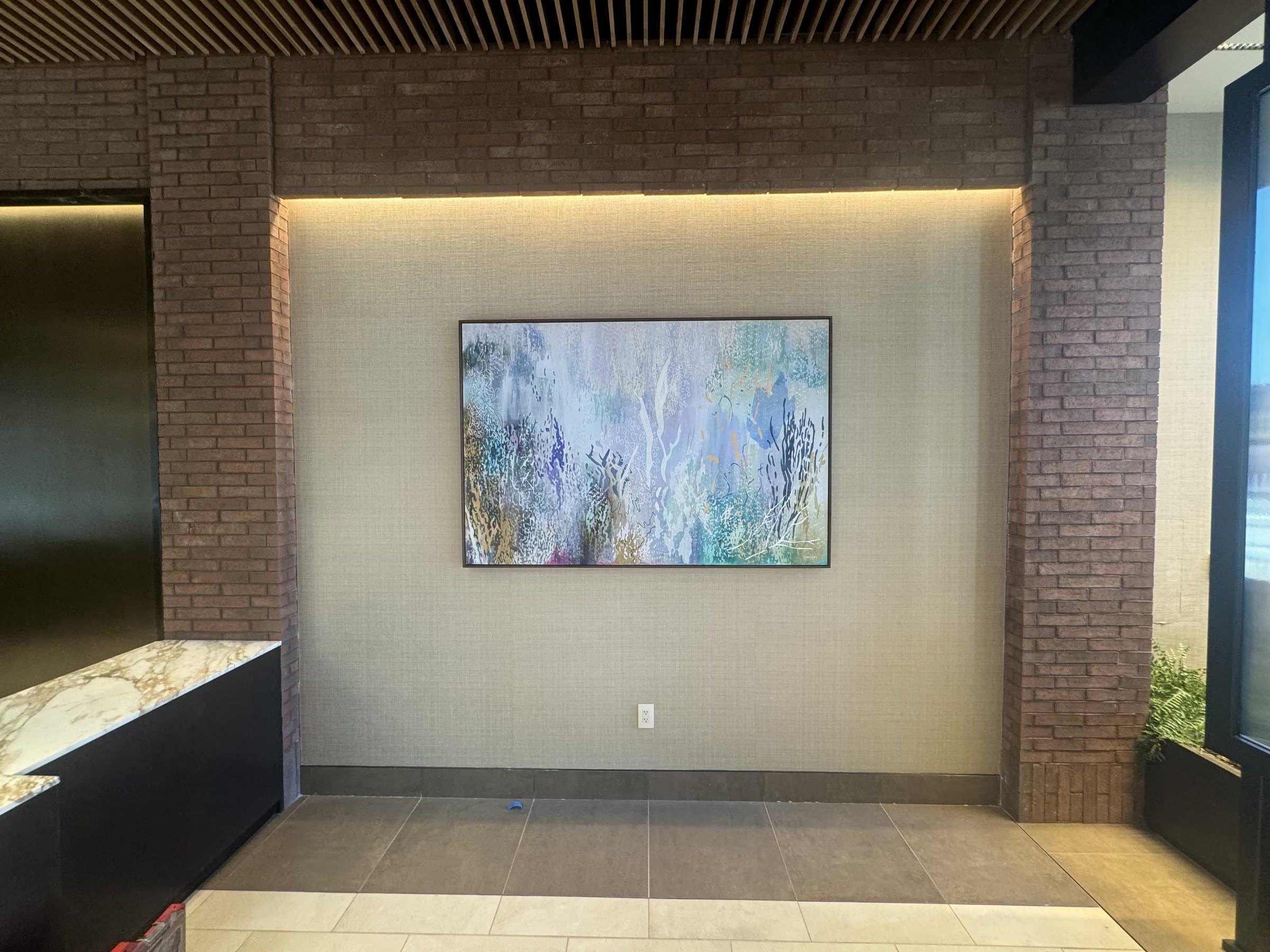 Blue, green and pale yellow abstract painting in an illuminated recess beside a reception counter