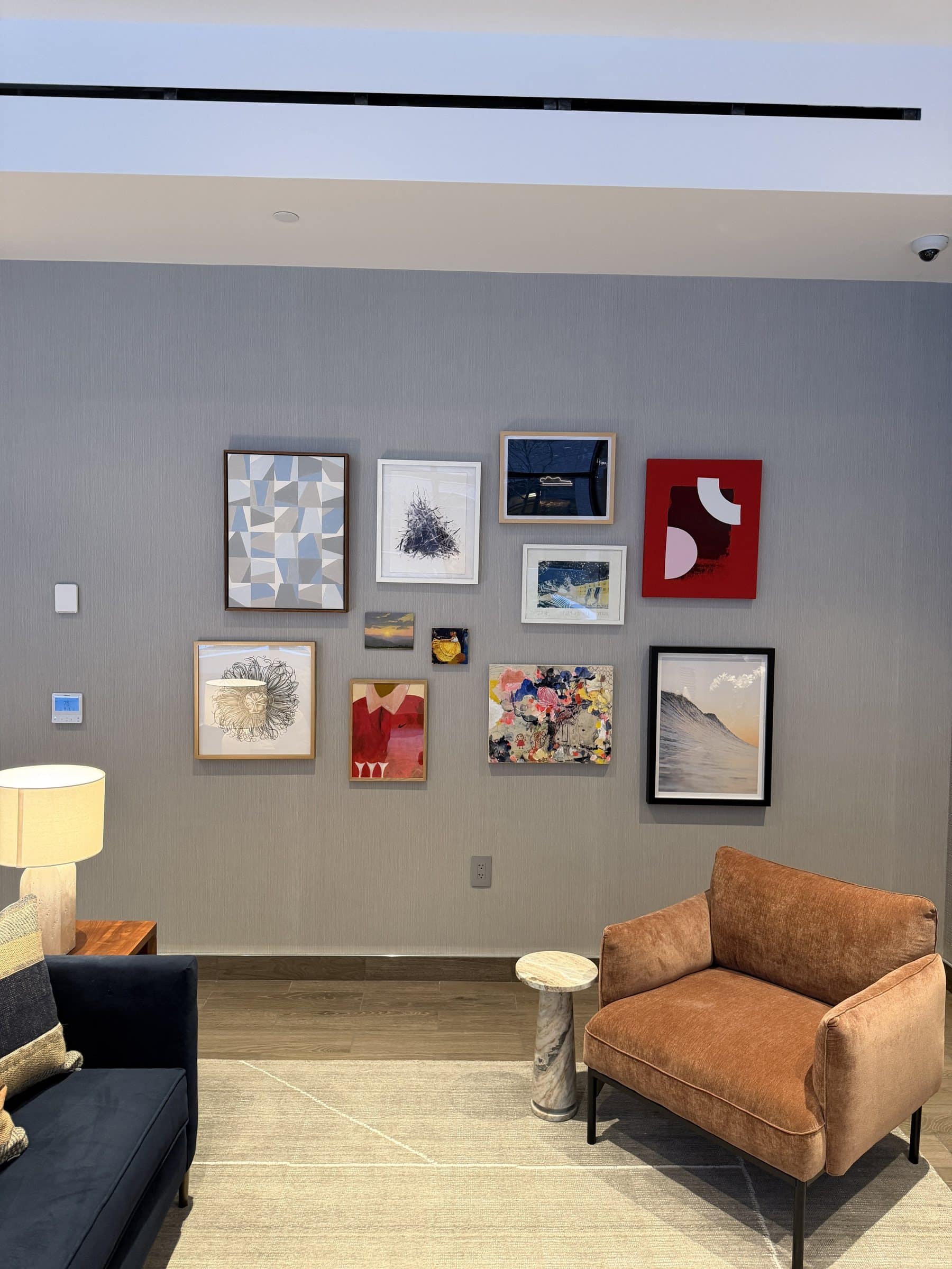 A group of small framed abstract works and photographs above lounge seating on a gray wall