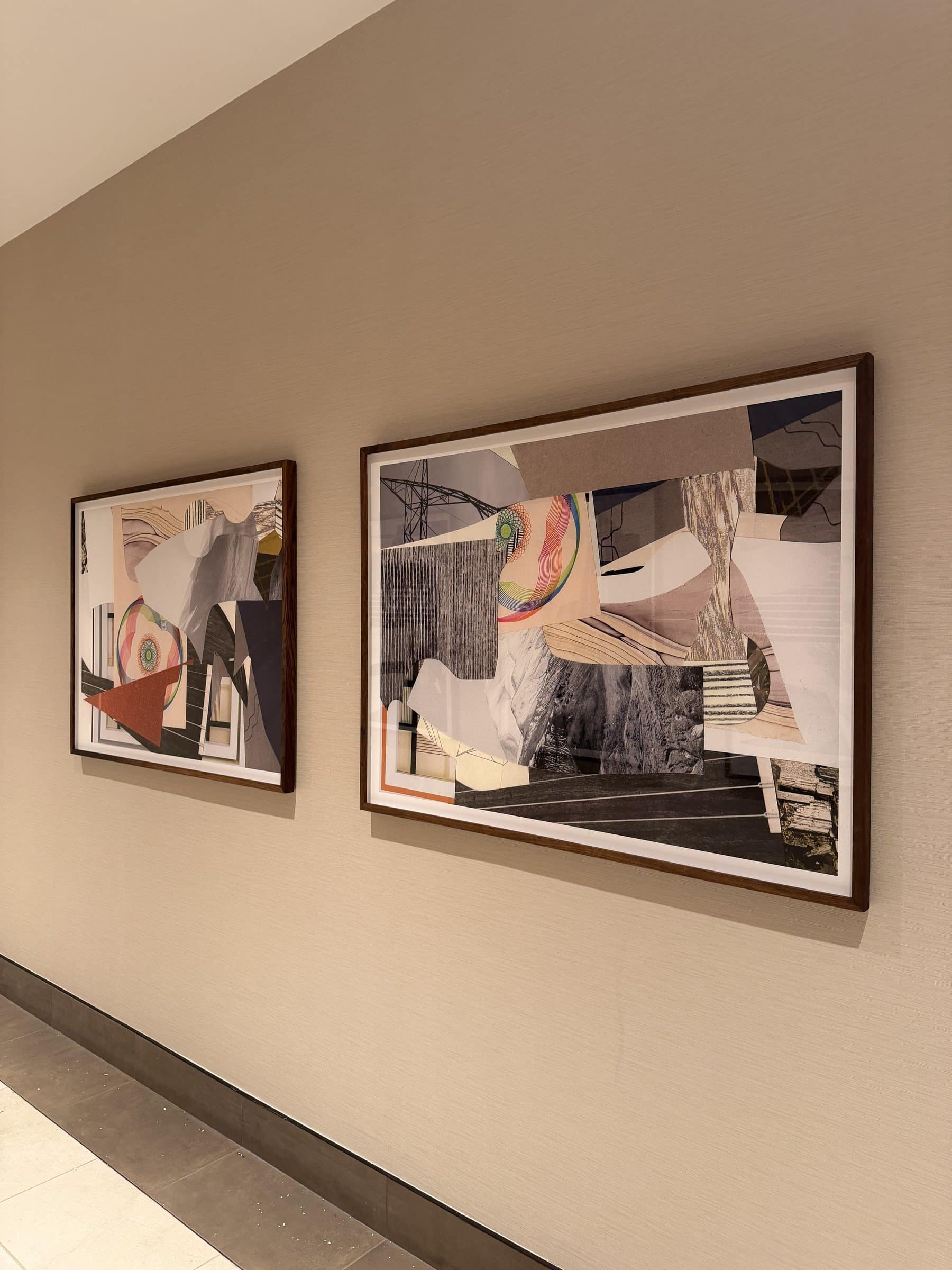 Two framed abstract collages with layered black, white and colored shapes along a corridor