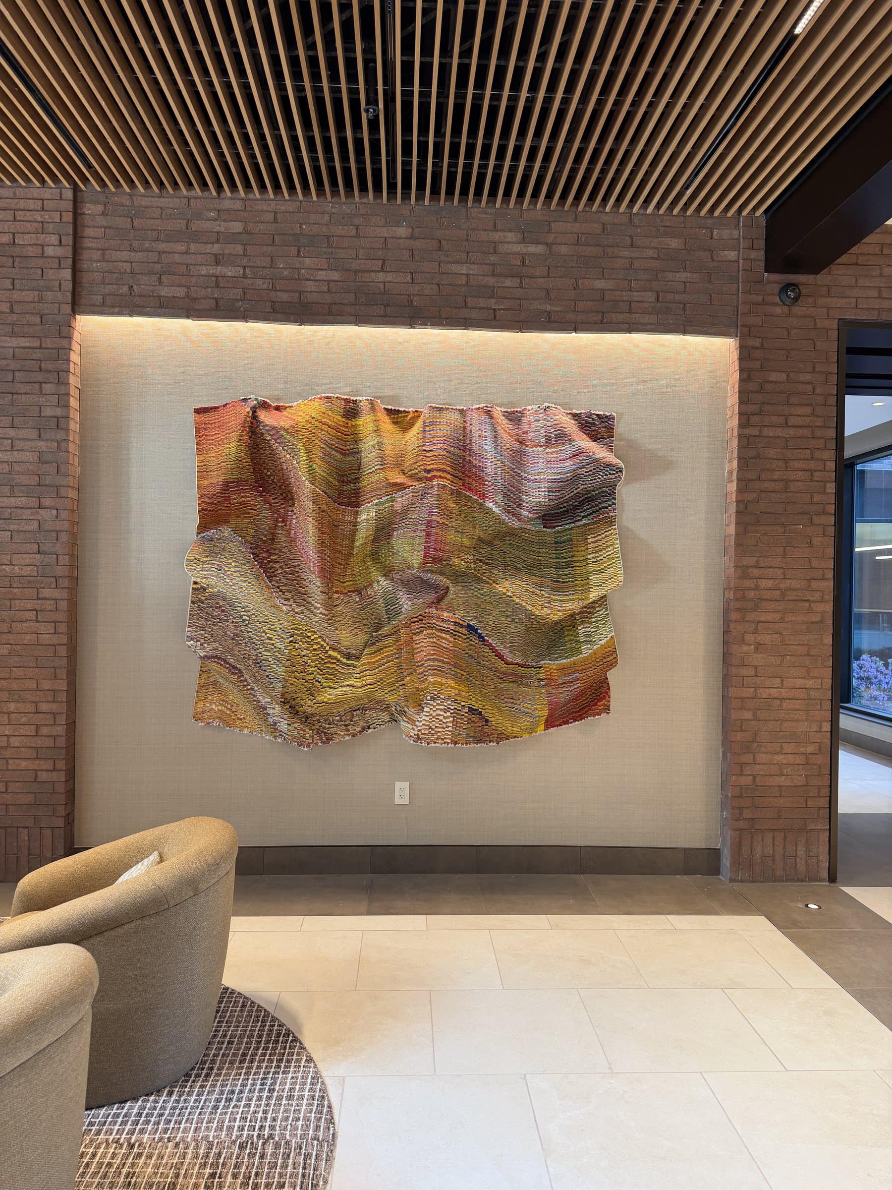 A rippling yellow, rose and green textile work fills a recessed lobby wall above a cream floor