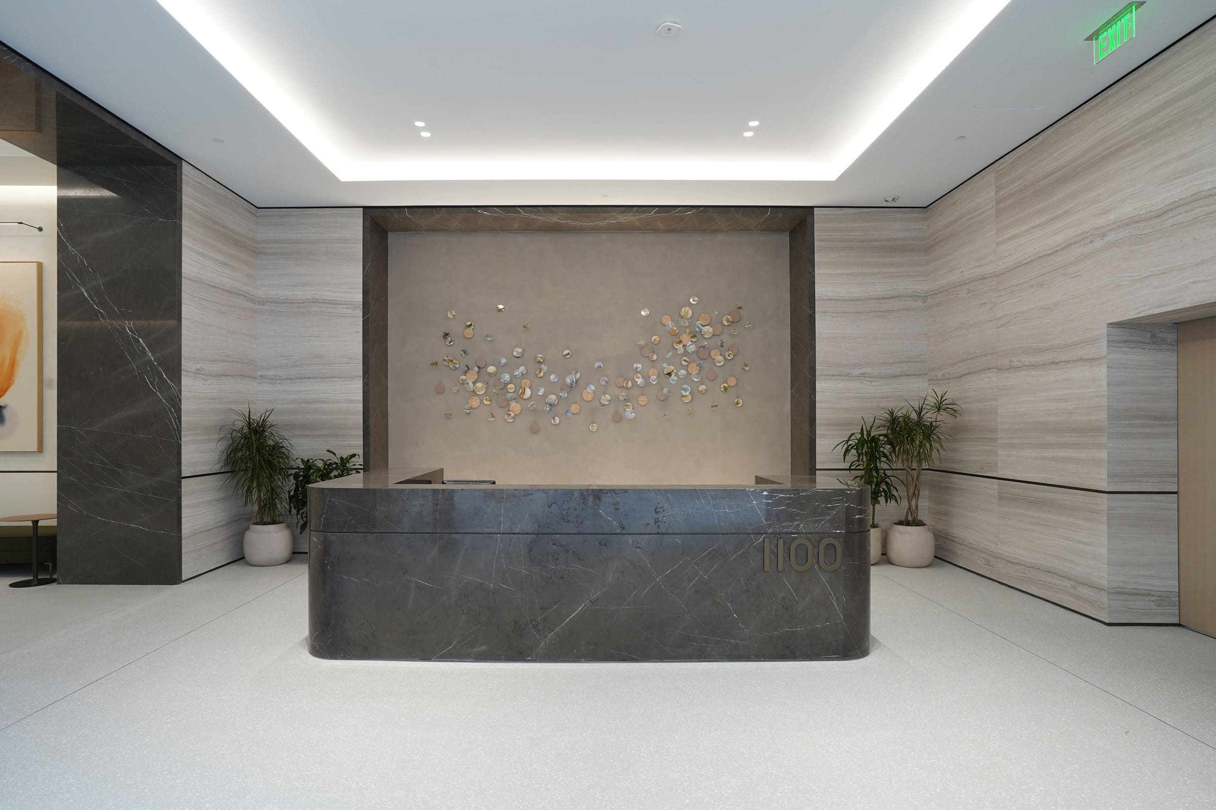Small circular and folded wall elements form a sweeping installation behind a dark stone reception desk