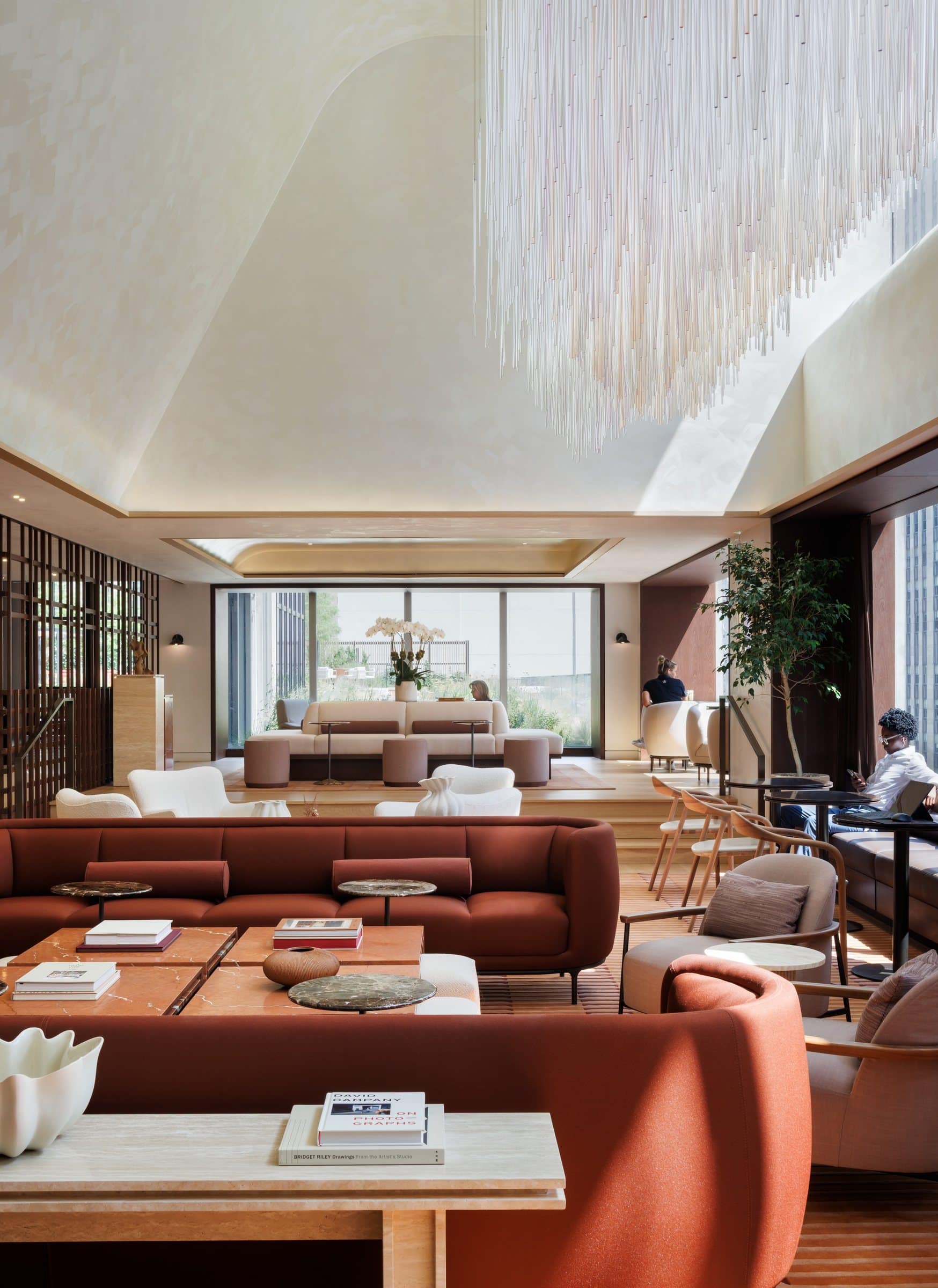 Fine transparent rods hang in a curved formation over an atrium lounge with rust sofas and pale armchairs