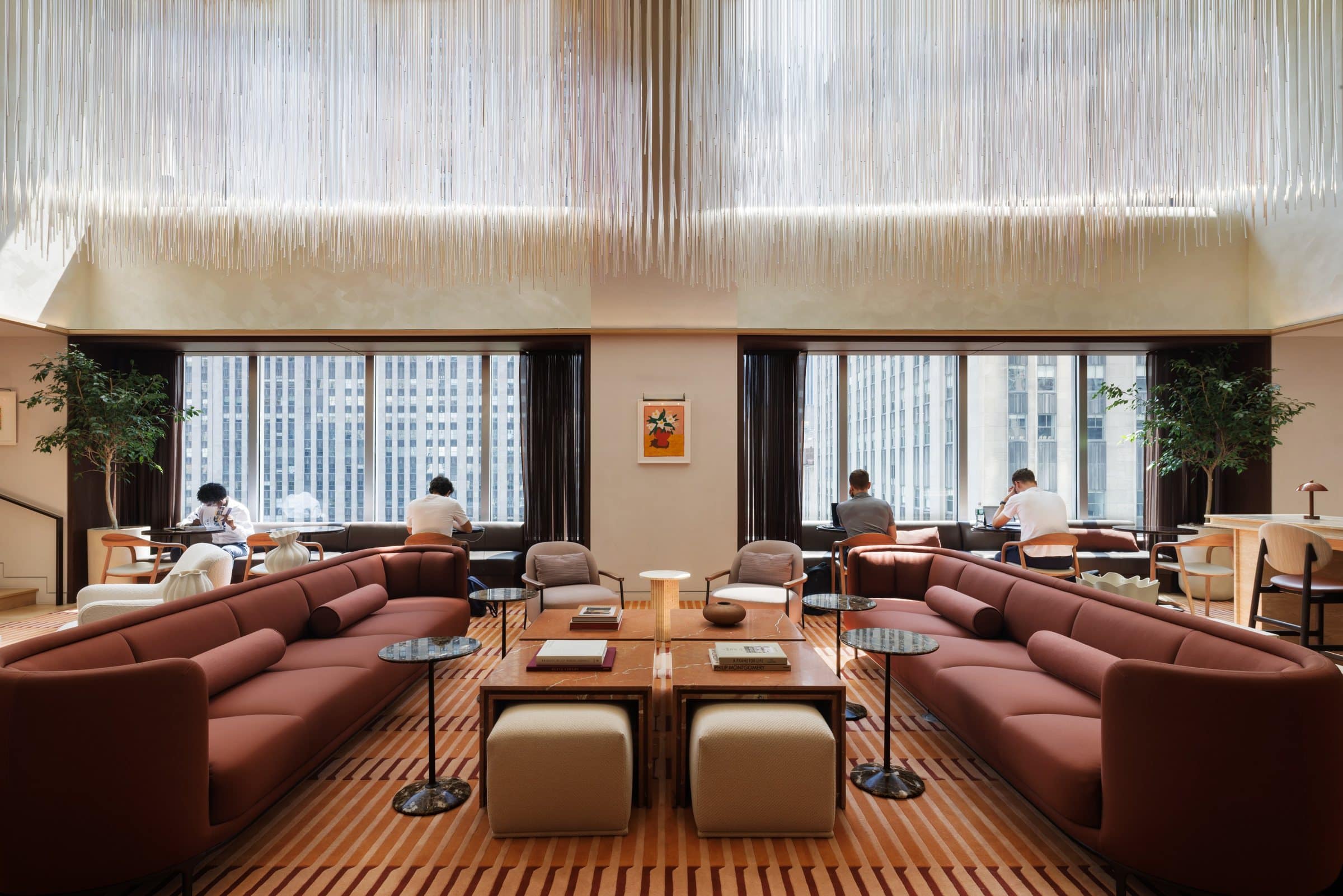 A suspended canopy of clear rods above rust sofas and occupied window-side tables in the atrium lounge