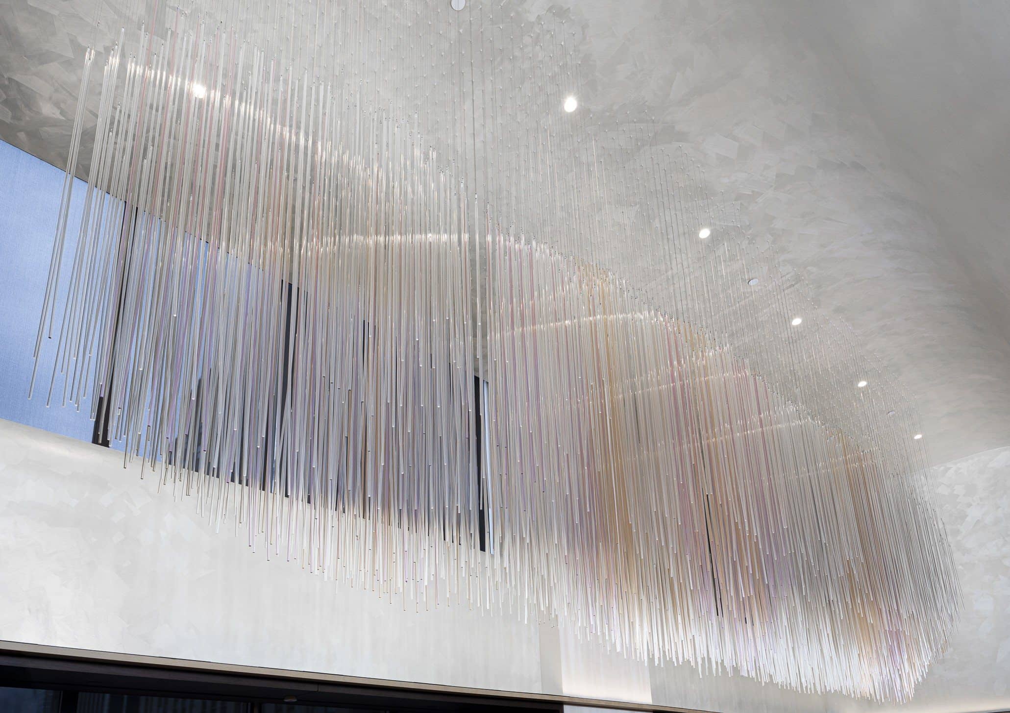 Upward view of hundreds of clear hanging rods forming an undulating canopy against a pale ceiling