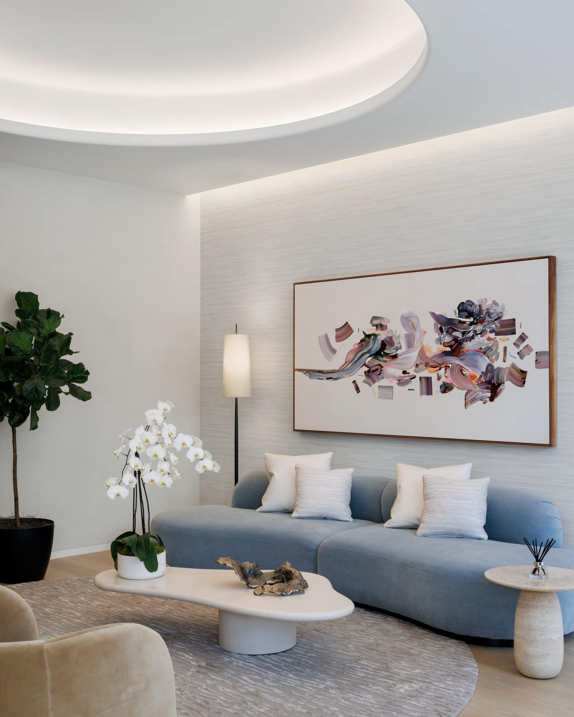 Curved pale blue sofa beneath a wide painting of lavender, gray, orange and brown brushstroke forms