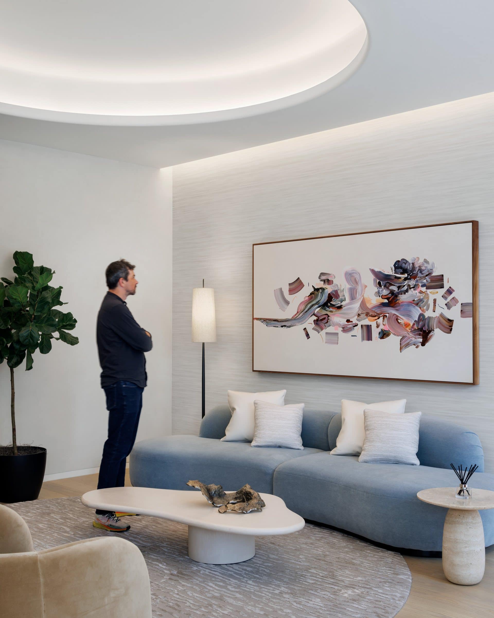 A visitor studies the wide brushstroke painting above the curved pale blue sofa