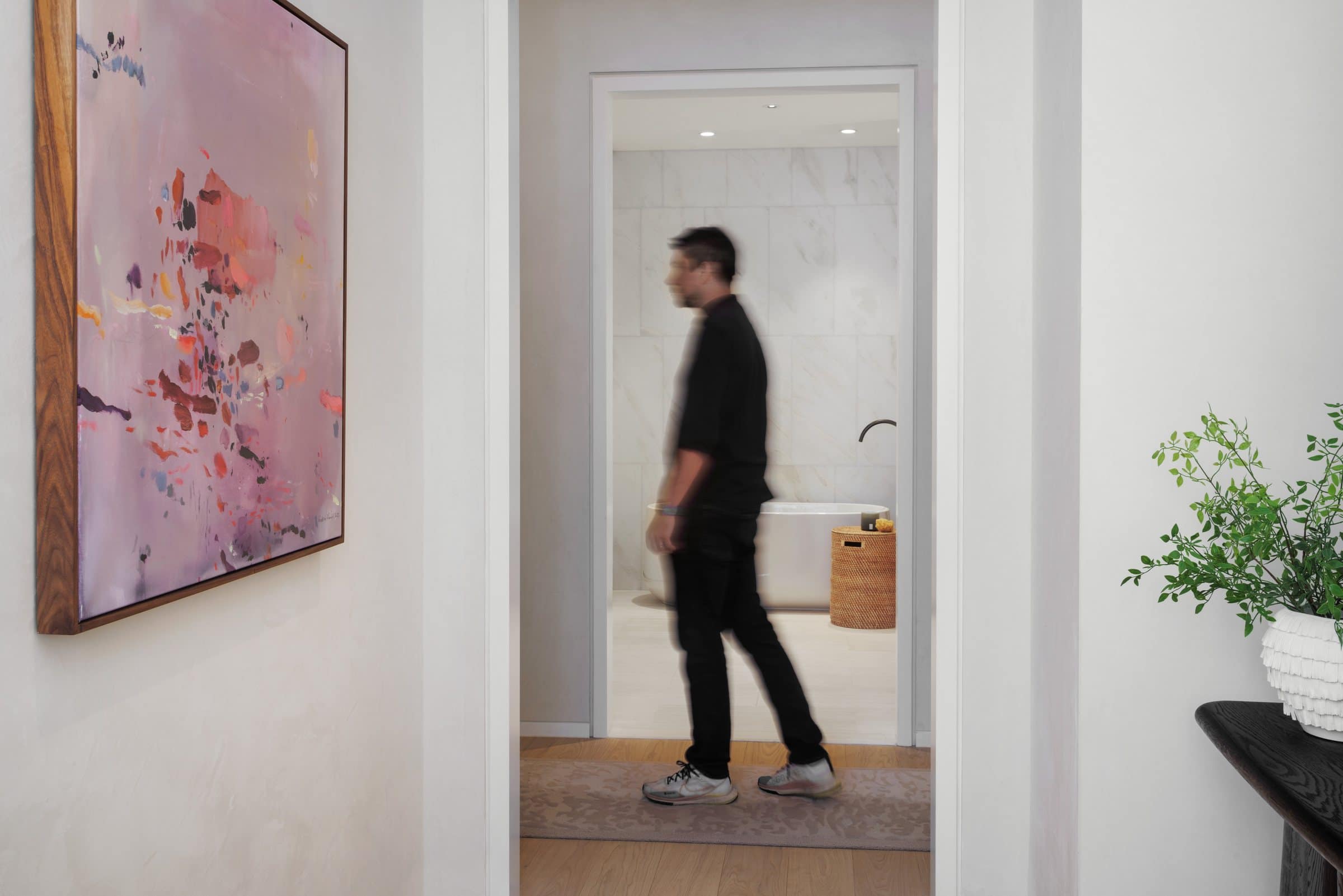 A visitor walks past the mauve abstract painting toward an open bathroom doorway