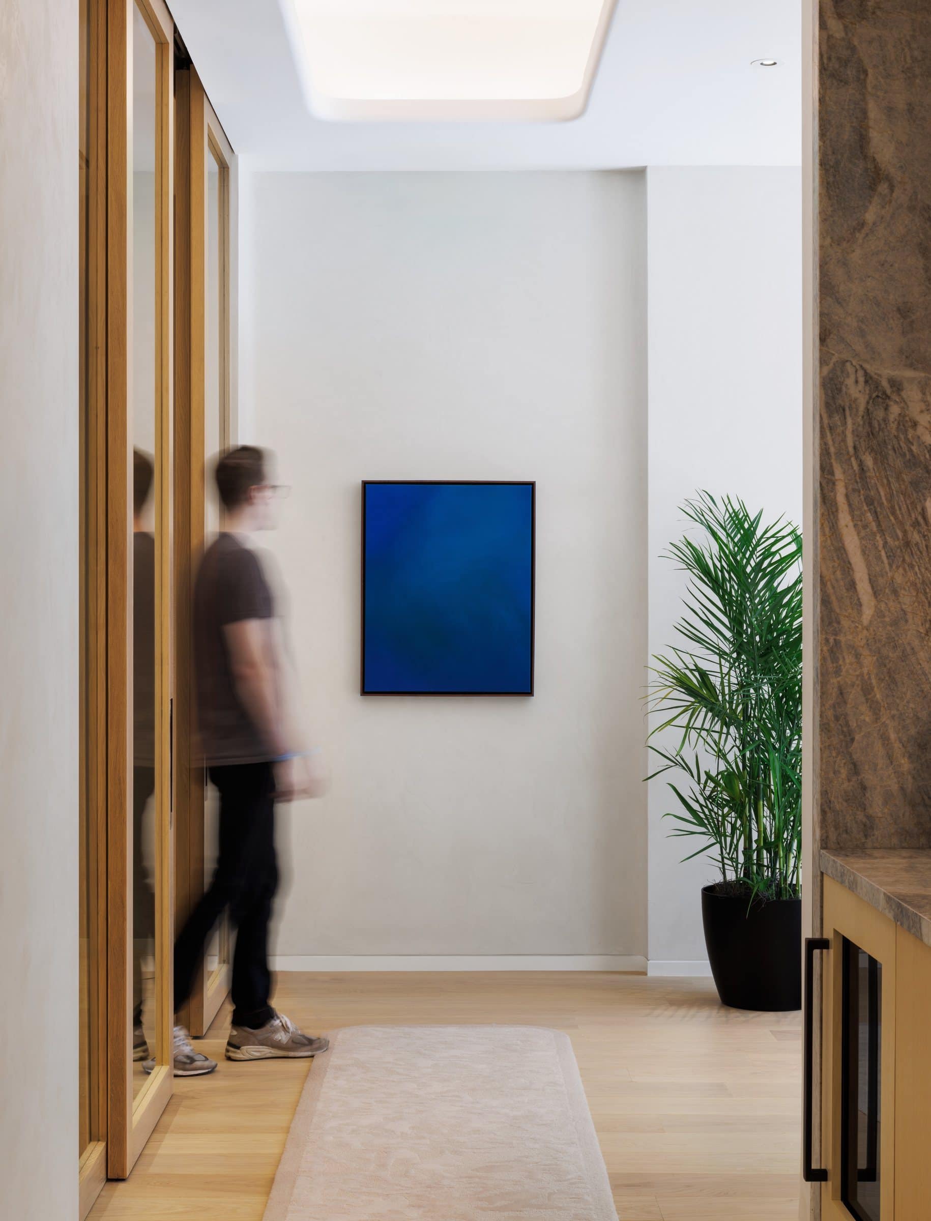 A visitor crosses the pale corridor beneath the deep blue color-field painting