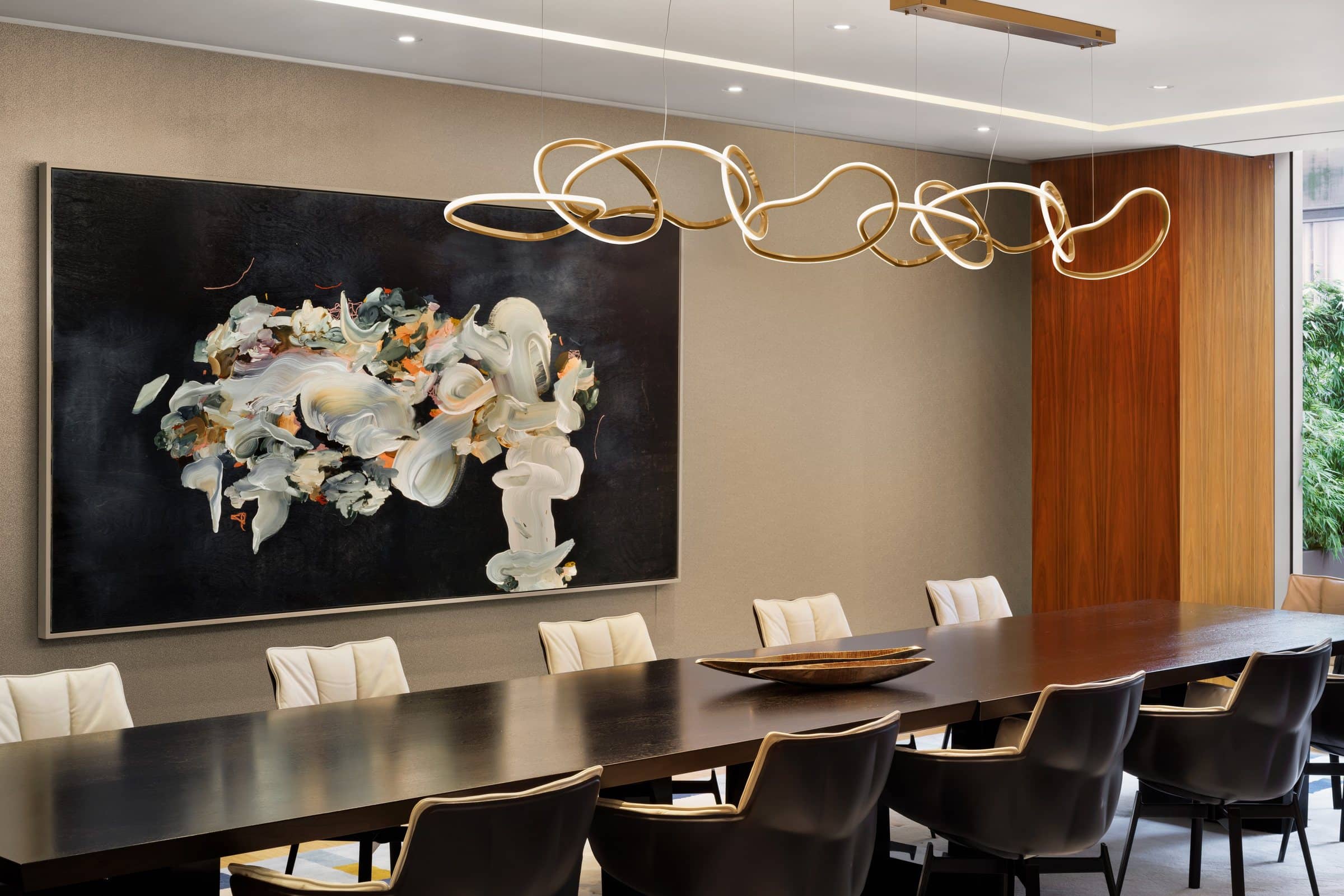 Long dining table beneath a large black-ground painting of swirling white, sage and orange forms