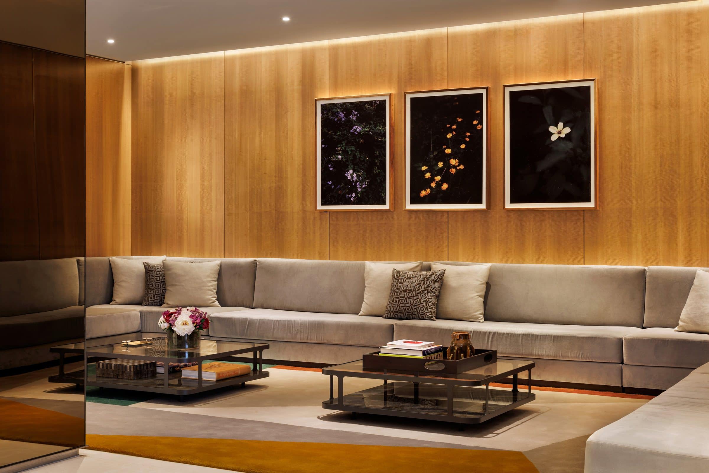 Gray sectional beneath three framed floral pictures on black against illuminated wood paneling