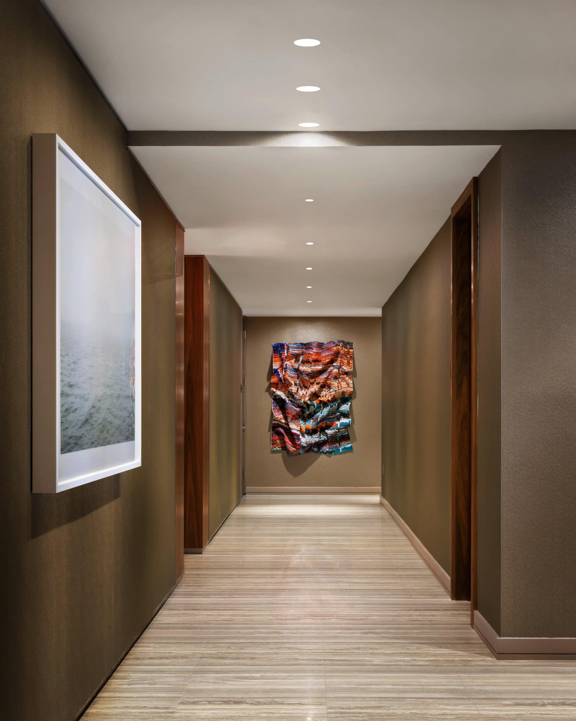 Corridor with a misty seascape photograph at left and a red, blue and orange cut-silk work at the far end