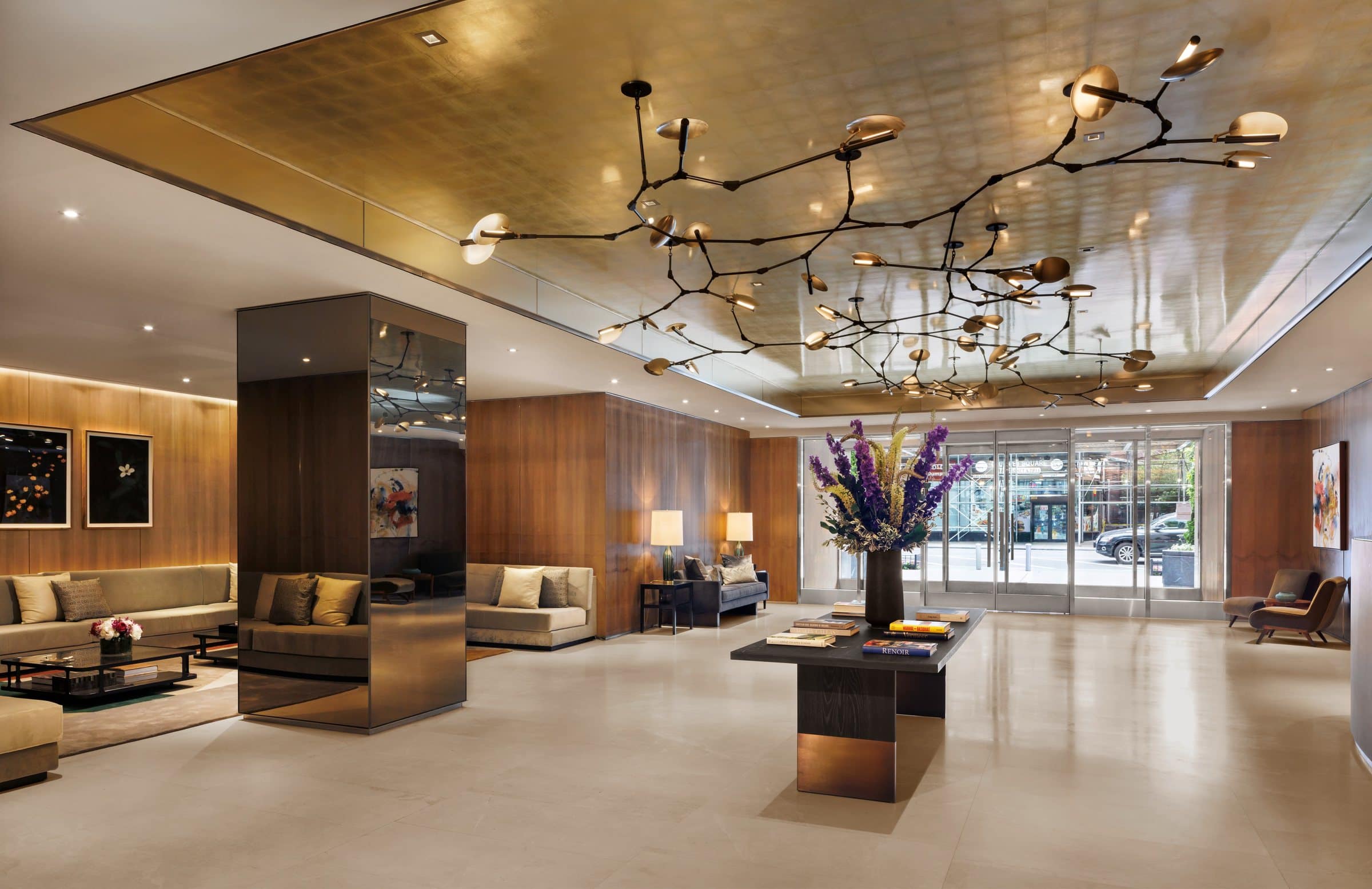 Wide lobby under a gold ceiling and branching chandelier, with floral pictures at left and a colorful abstract near the entry