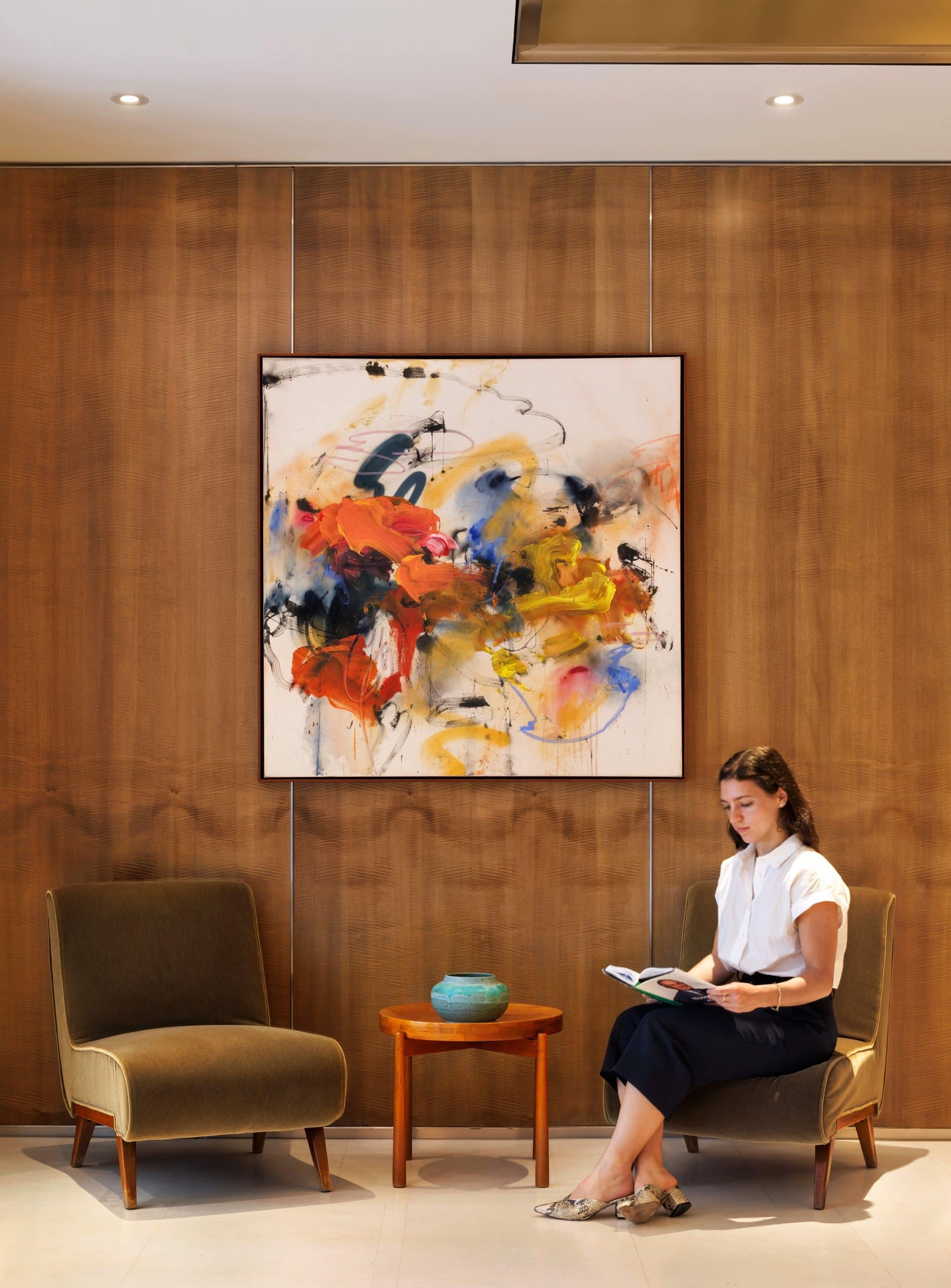 A visitor reads below the orange, yellow and blue abstract painting in the oak-paneled lobby nook