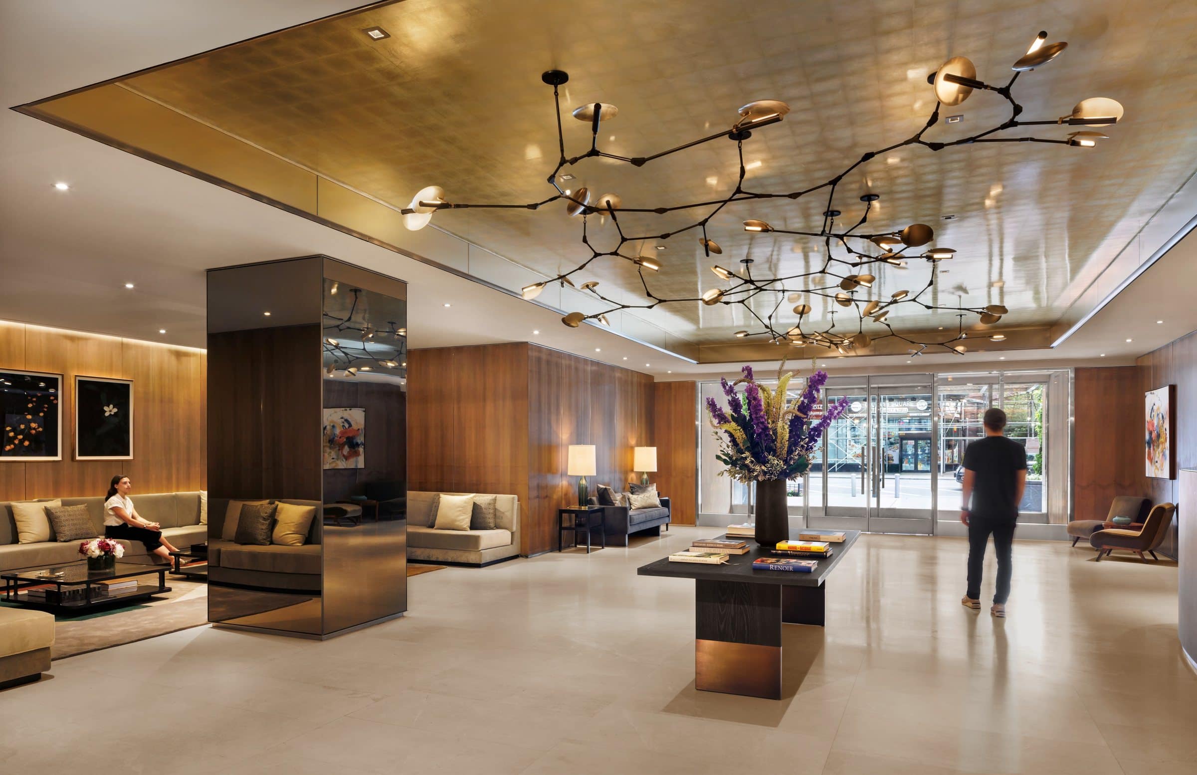Visitors give scale to the gold-ceilinged lobby, with floral pictures above sofas and a colorful abstract at the entry