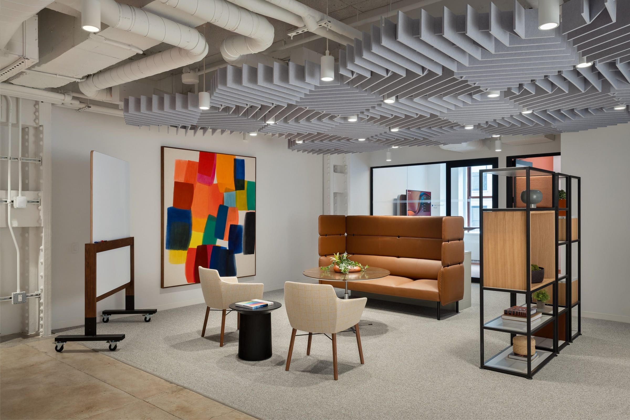 Large painting of overlapping translucent color blocks in orange, red, blue and yellow above a seating area under a sculpted felt ceiling