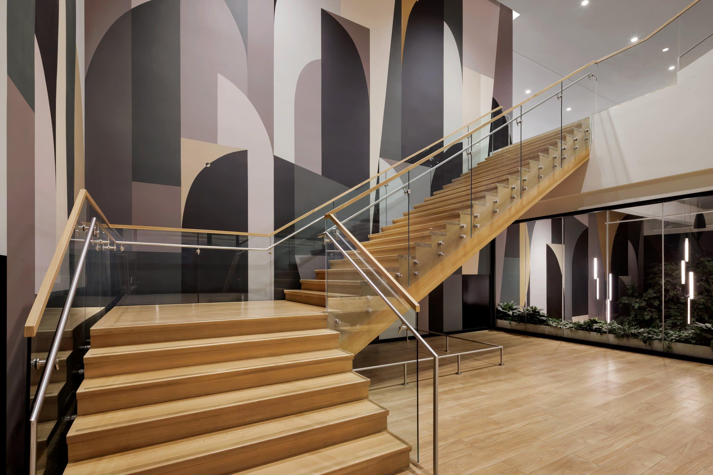 A large geometric mural in gray, cream, black and pale pink wraps the walls around a wood stair
