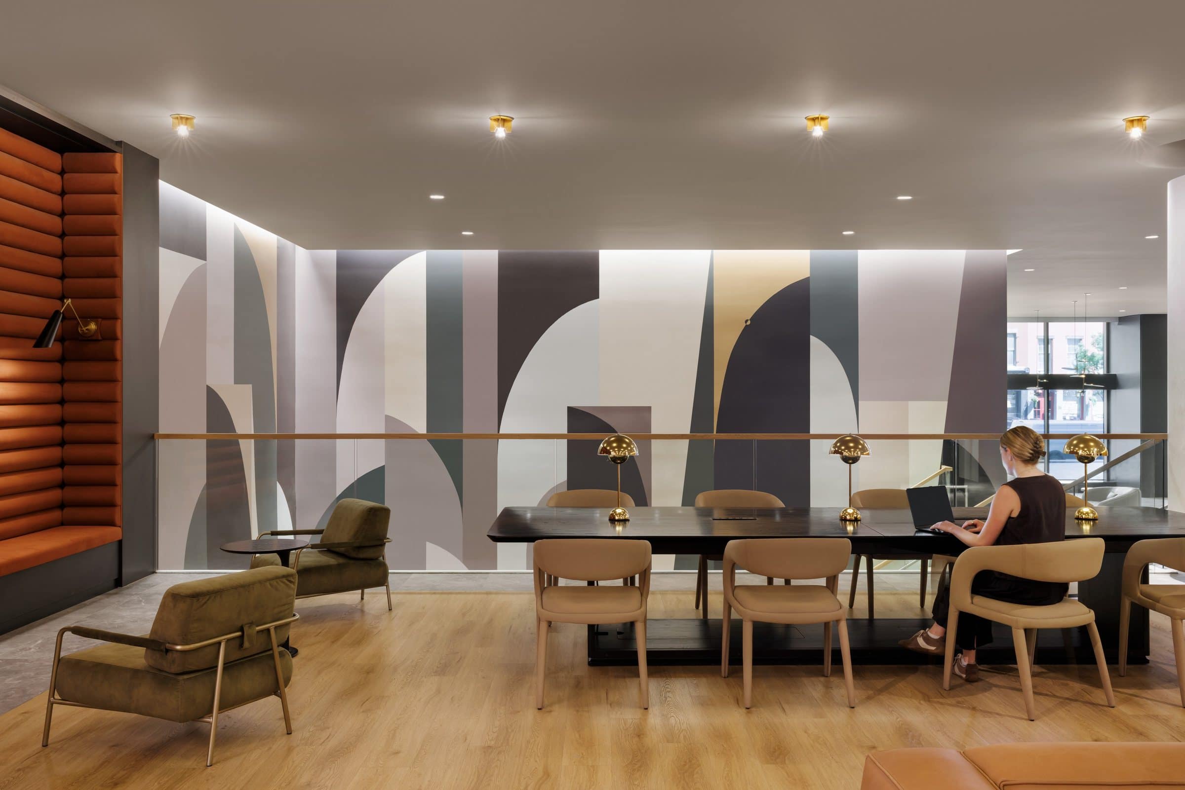 A person works at a long table beside a glass balustrade and the geometric atrium mural