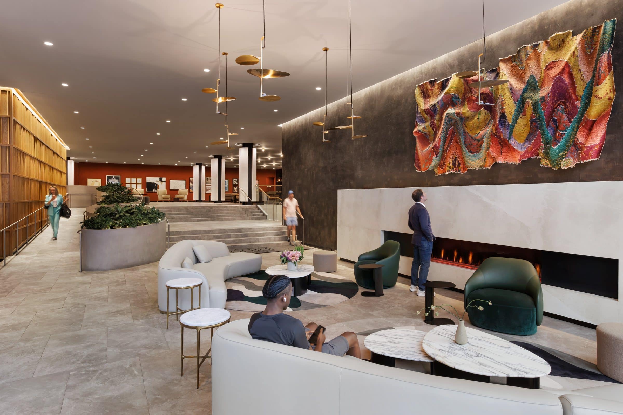 Visitors use the lobby seating beneath the rippling textile work, with the gallery wall visible beyond