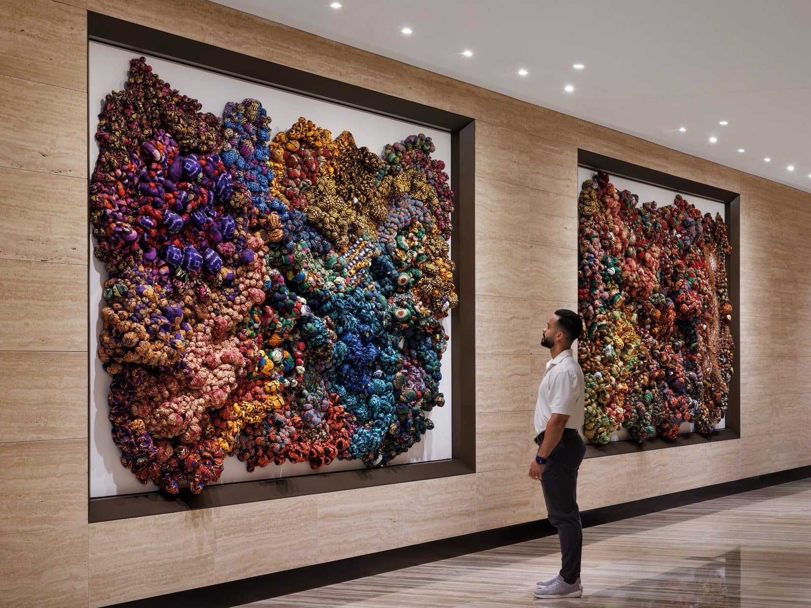A man stands before two large knotted-fabric wall works in a stone-clad corridor