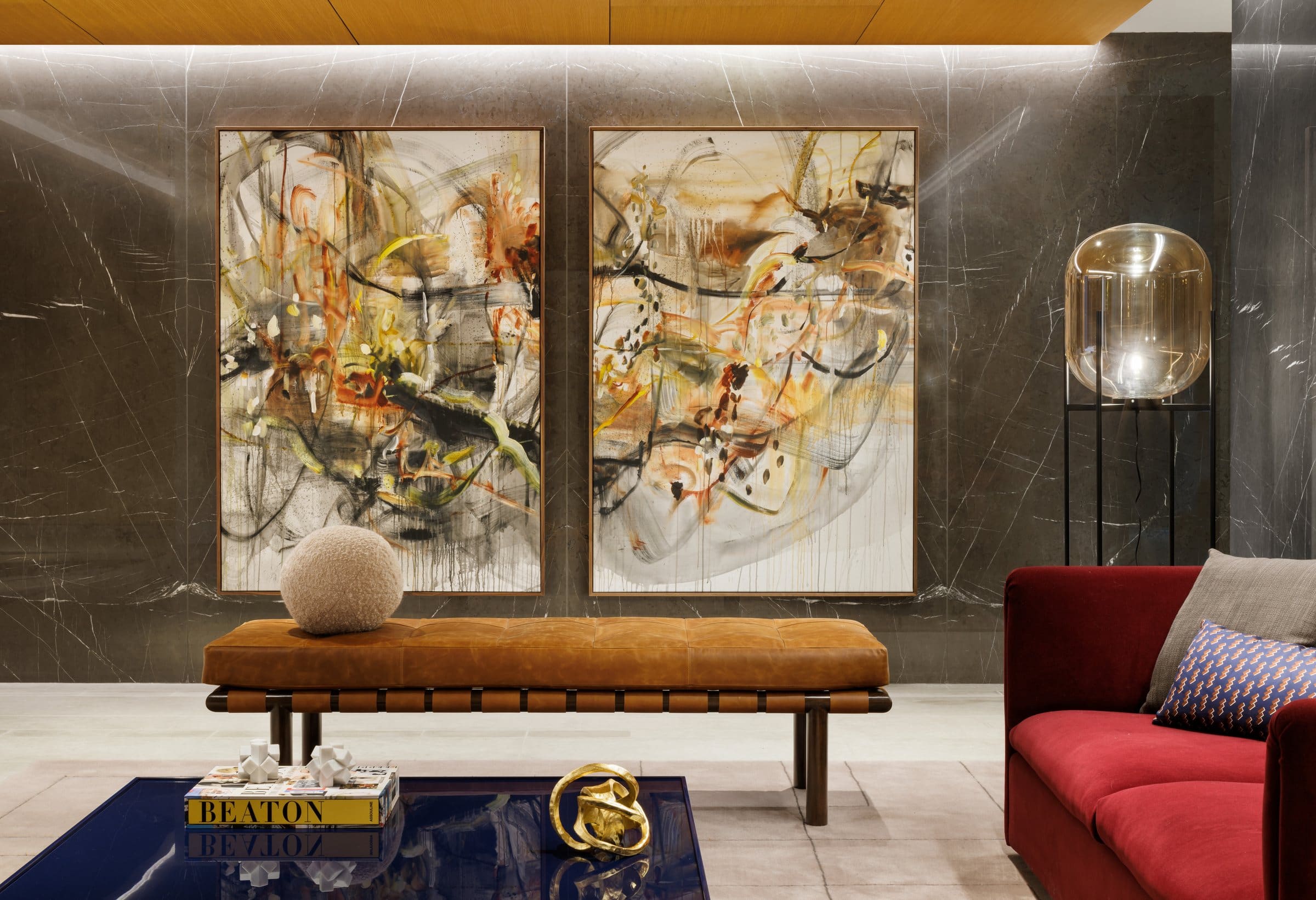 Two tall ochre, rust and black gestural paintings above a leather bench against dark marble