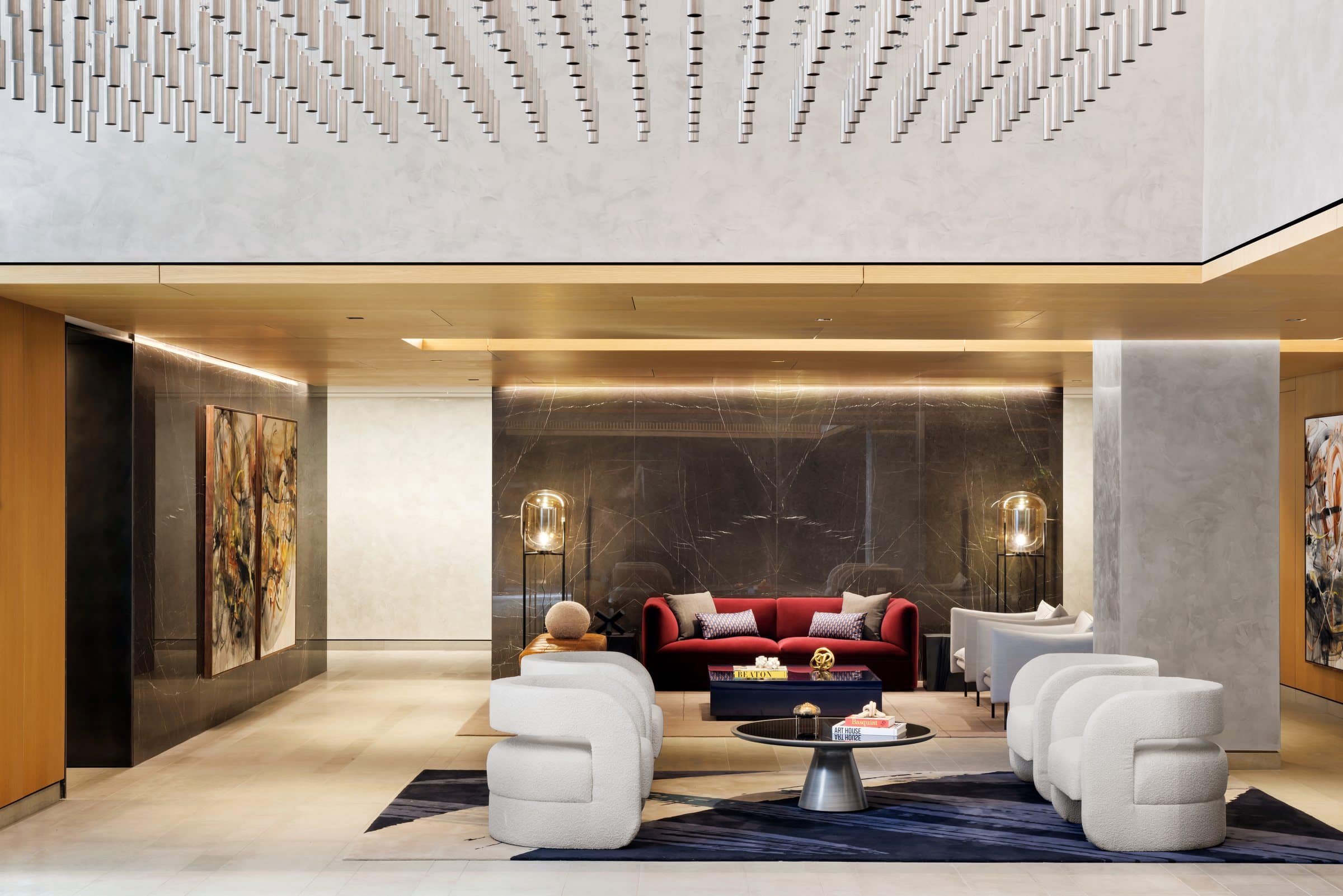 Double-height lounge with white armchairs, a red sofa and tall gestural paintings on either side