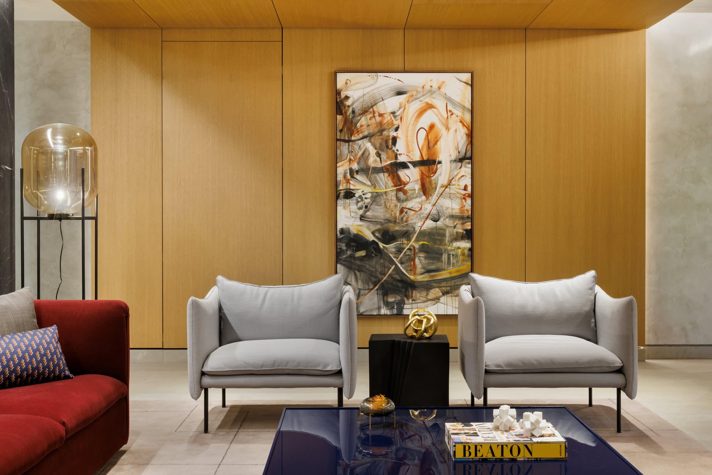 Two gray armchairs beneath a tall ochre and black gestural painting on a wood-paneled wall