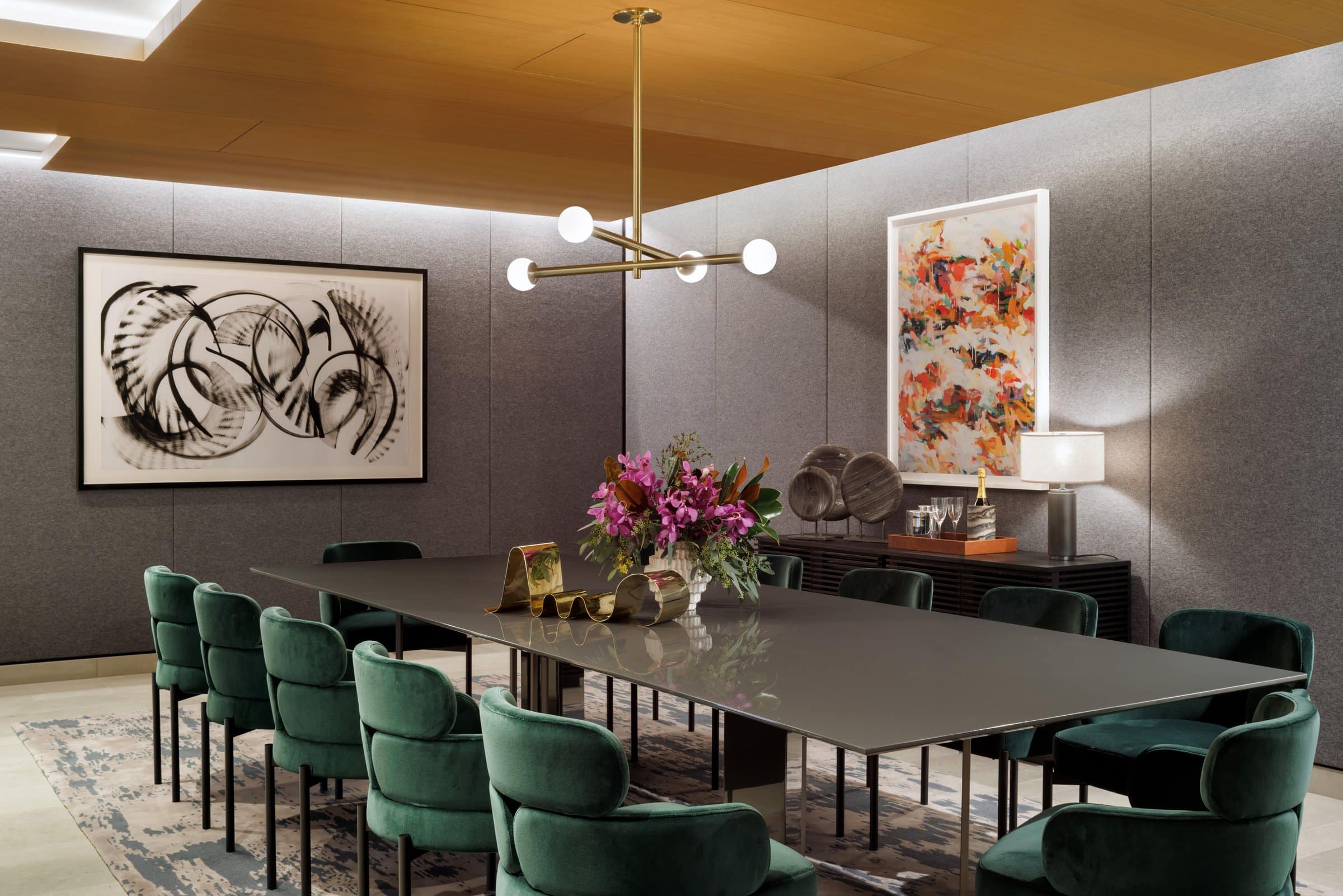 Private dining room with green velvet chairs, a wide black ink work and a colorful vertical abstract painting