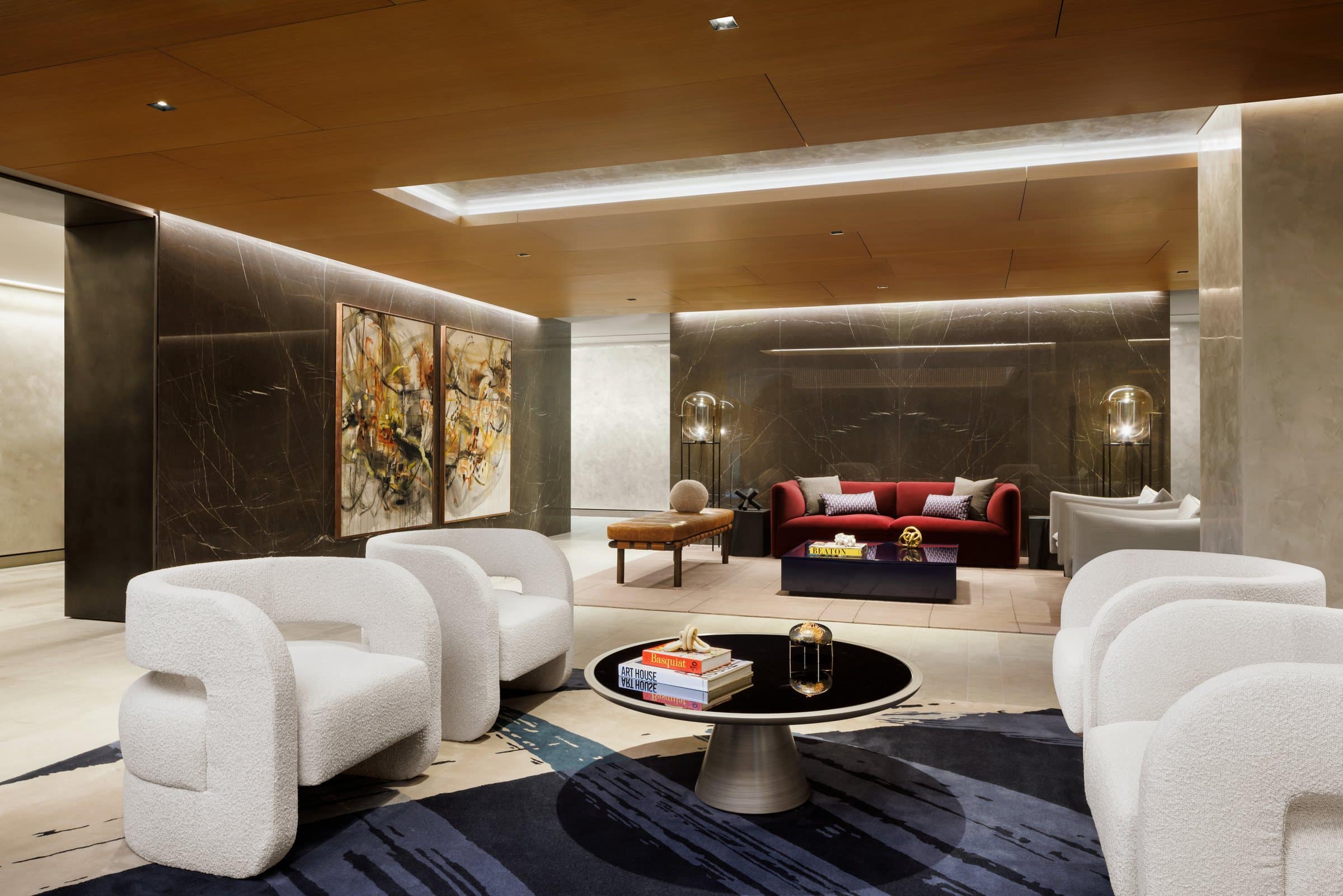 Angled view of a double-height lounge with white armchairs, a red sofa and paired ochre and black paintings