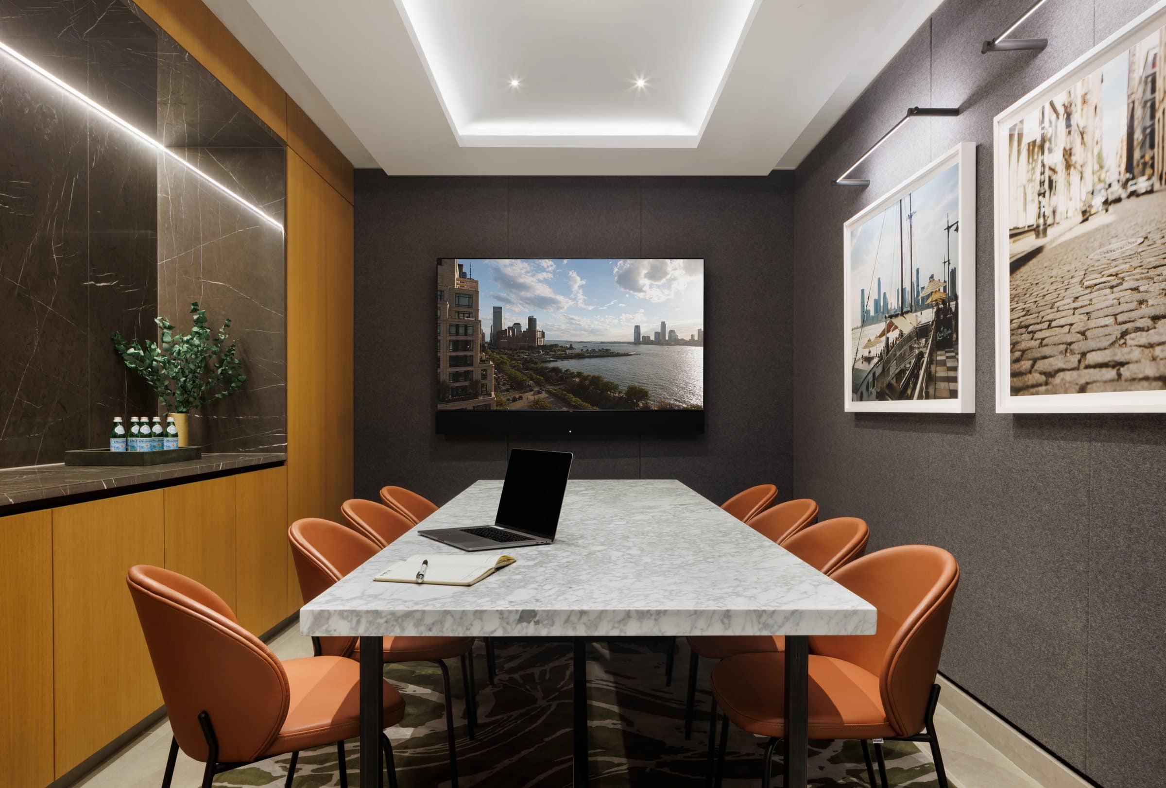 Conference room with orange chairs and framed neighborhood photographs beside a wall-mounted screen