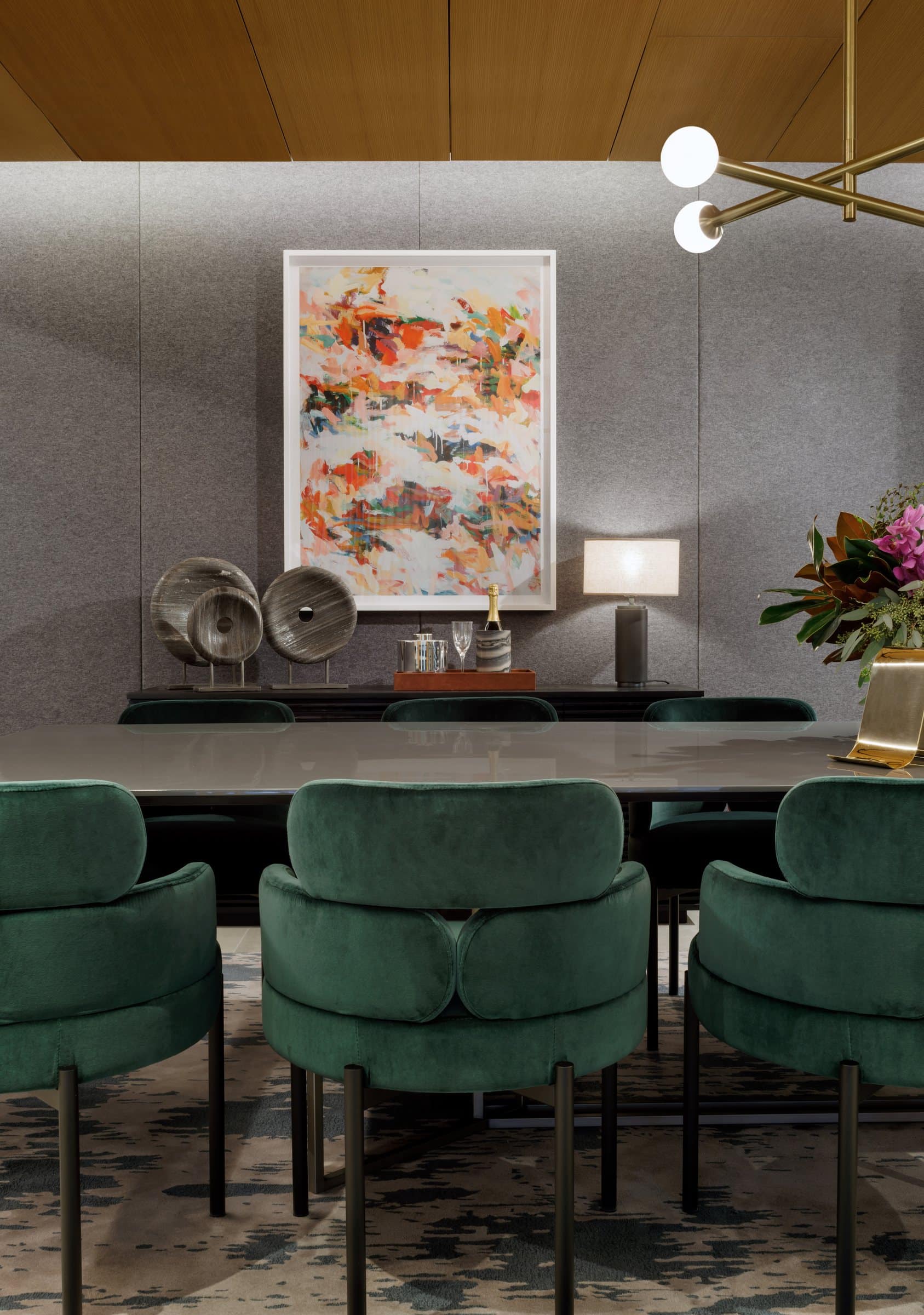 A colorful vertical abstract painting above a sideboard at the end of a green-chaired dining table