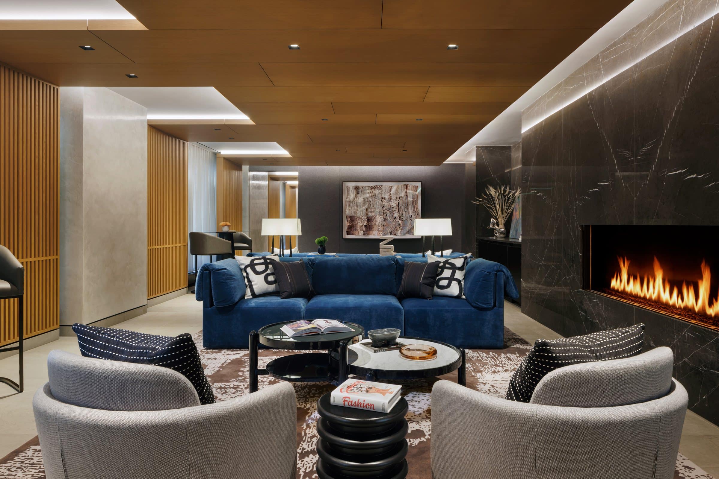 Navy sofa and gray armchairs beside a marble fireplace, looking toward a framed rippling textile work