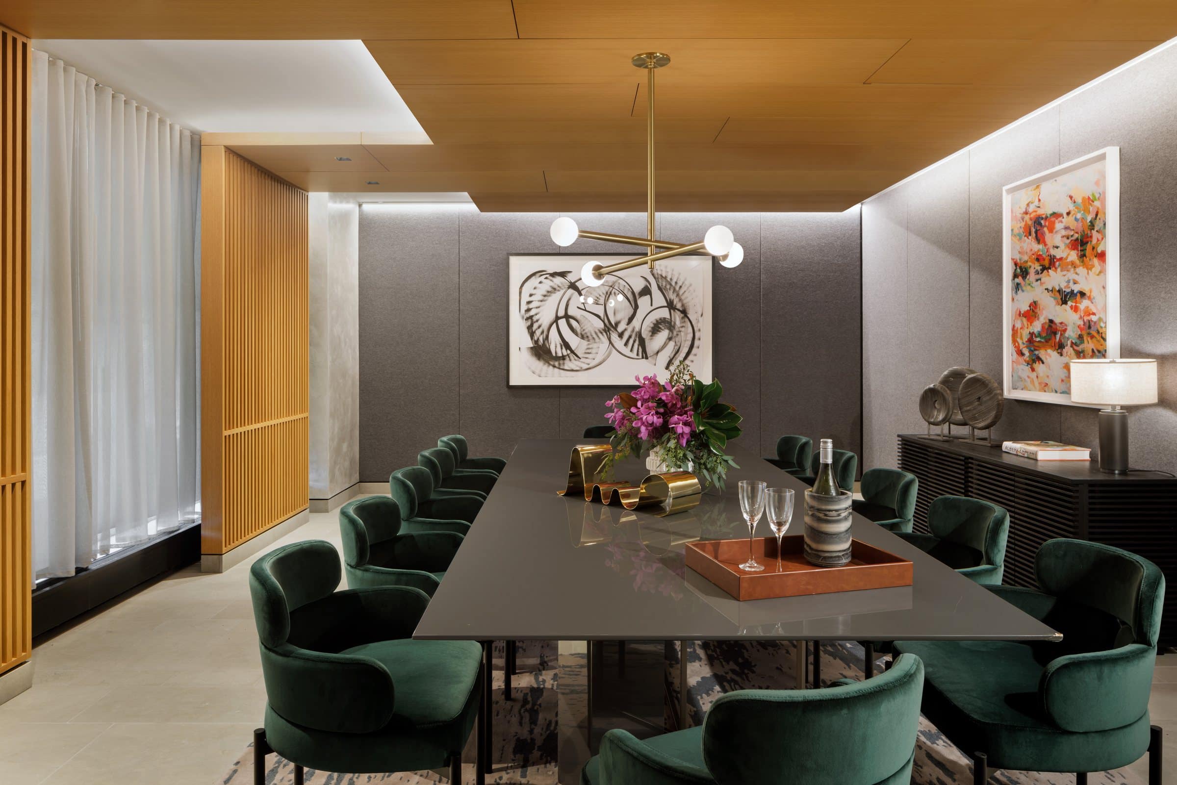 Long private dining table with green velvet chairs, a black gestural work at the end and colorful painting at right