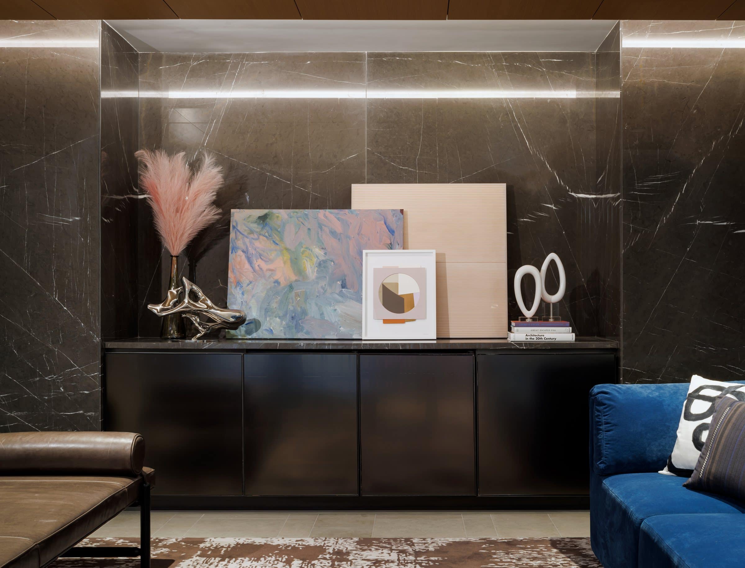 Three artworks lean on a credenza in a dark marble niche: a pastel abstract, a peach line painting and a small geometric print