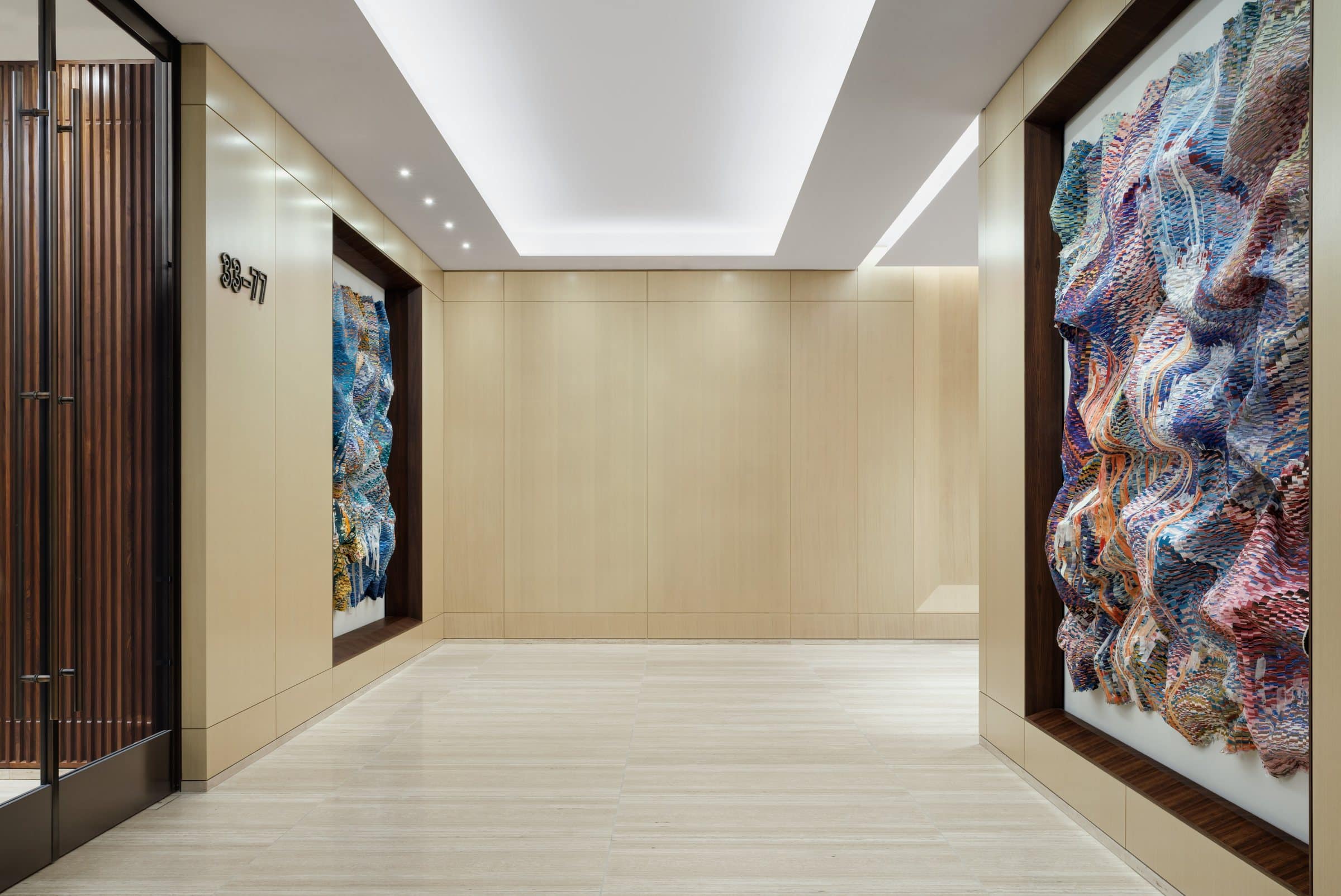 Sky-lobby corridor with a blue-and-gold textile work at left and a pink, lavender and blue textile work at right