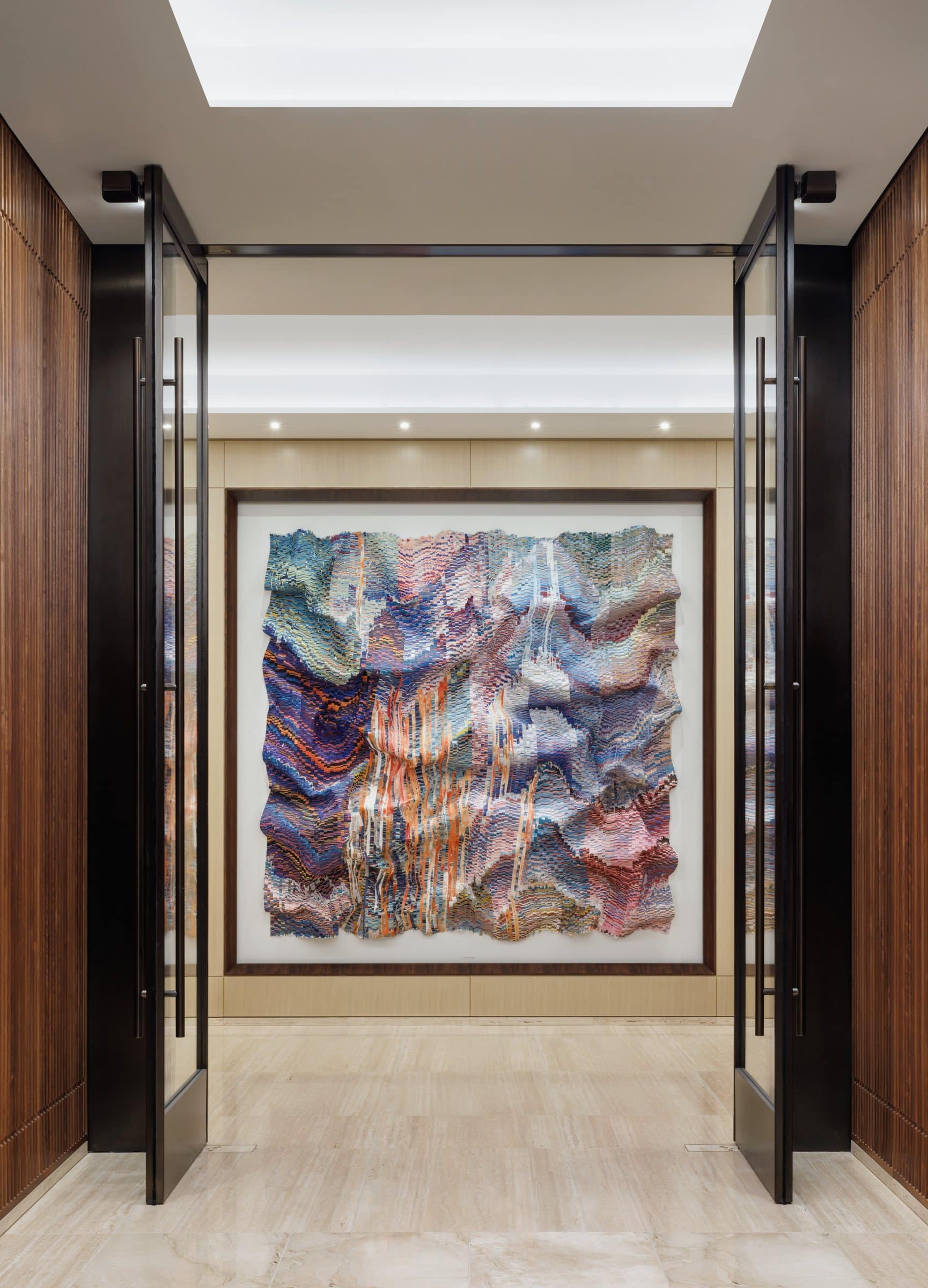 Open glass doors frame a pink, lavender, blue and orange cut-silk work at the end of an elevator corridor