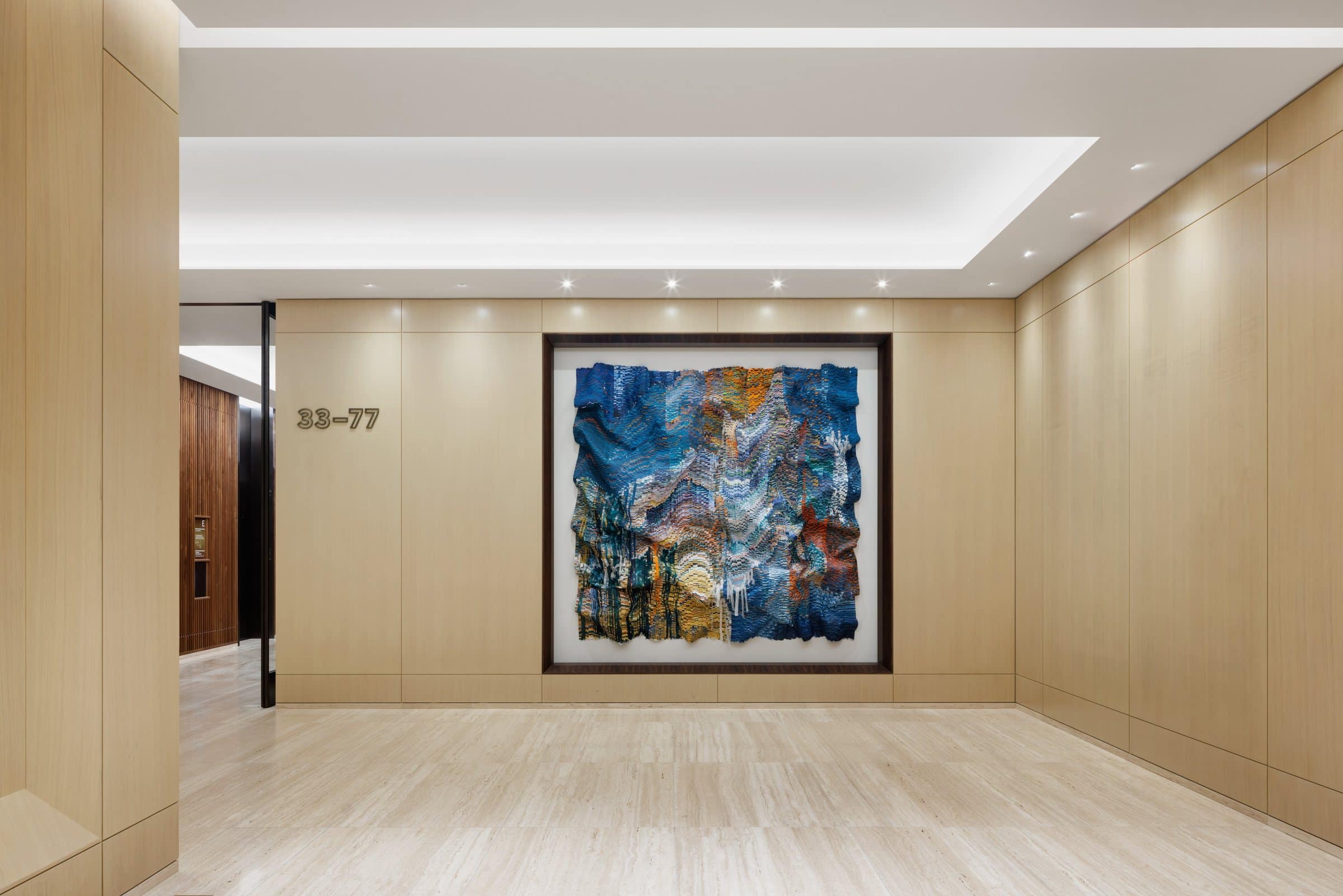 Wide wood-paneled corridor facing a blue-and-gold cut-silk work in a recessed dark frame