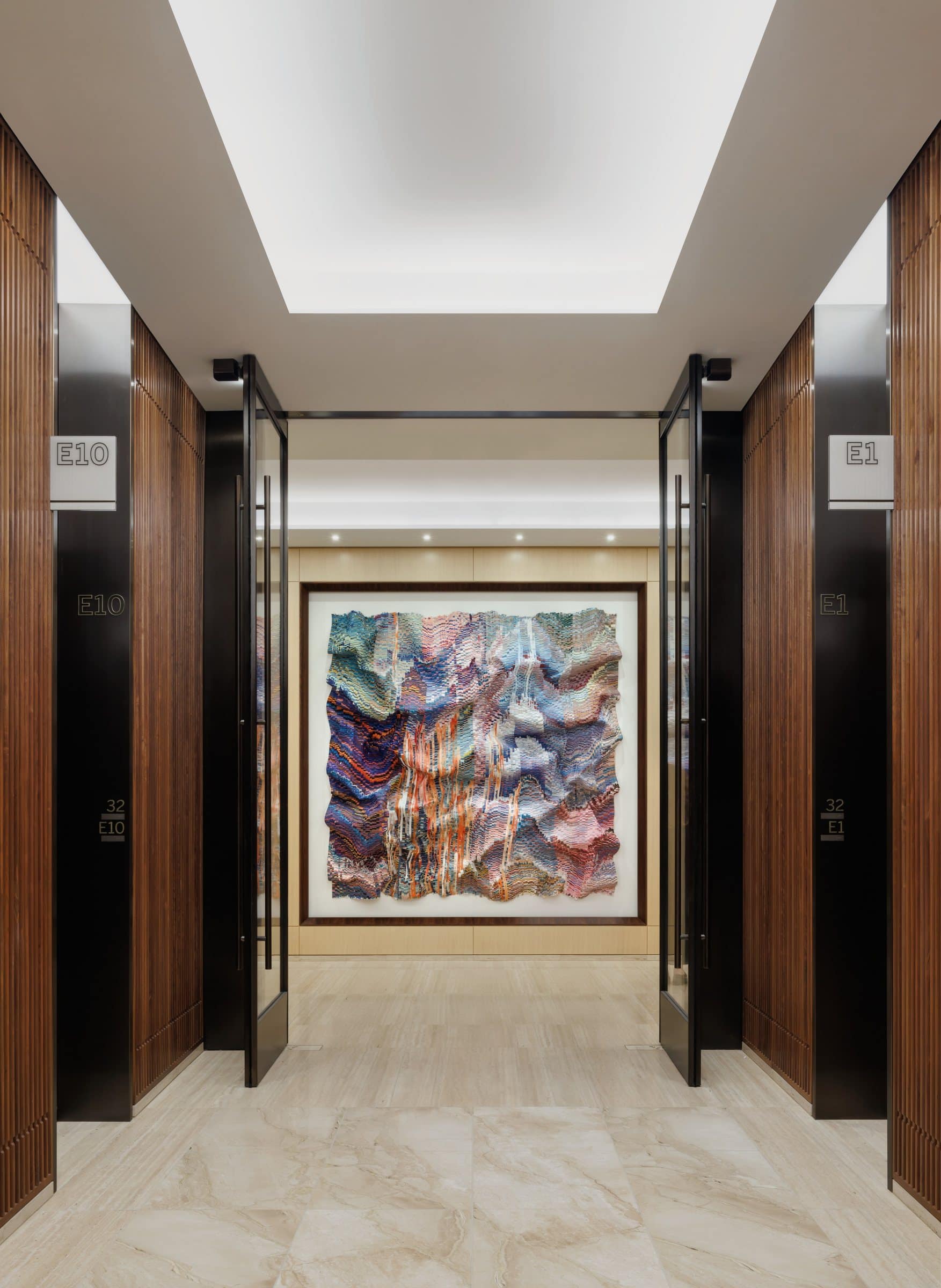 View between elevator doors toward a large rippling textile work in lavender, blue, pink and orange