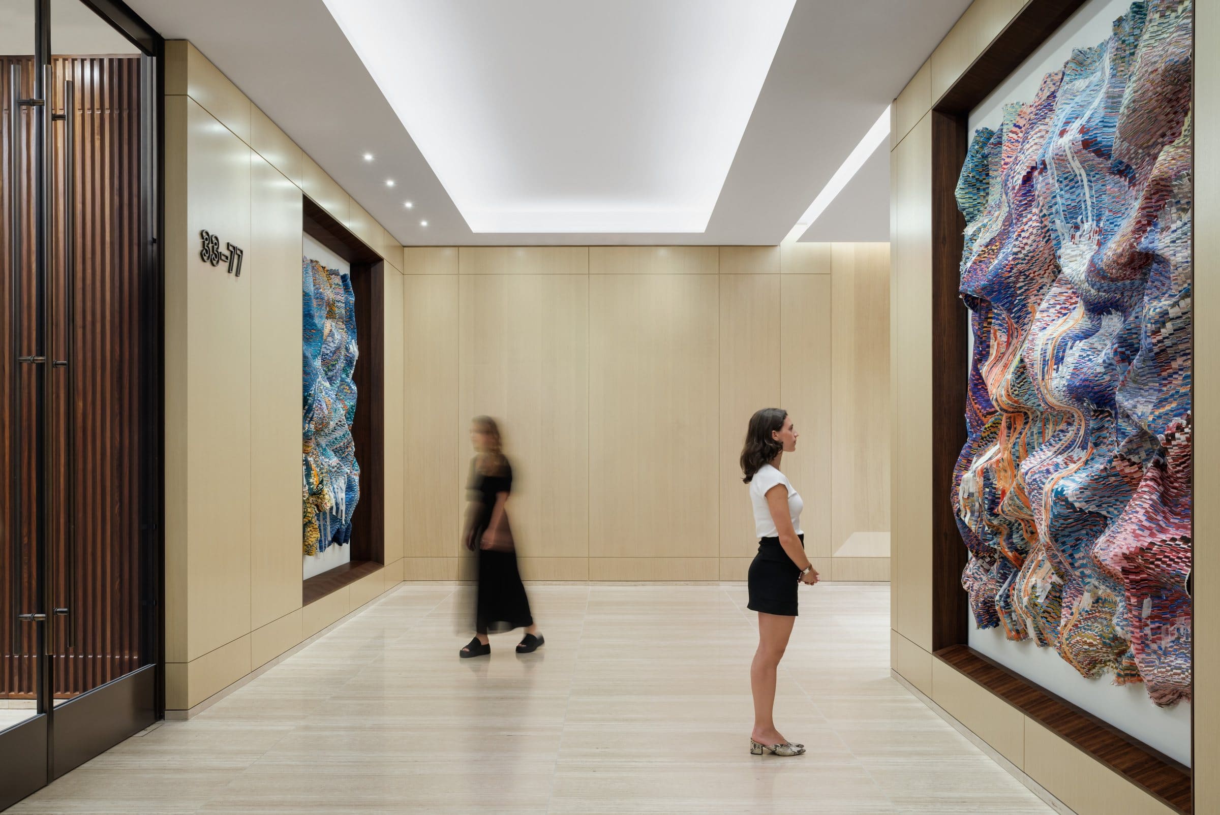 Two visitors give scale to the large rippling textile works on opposite sides of the sky-lobby corridor