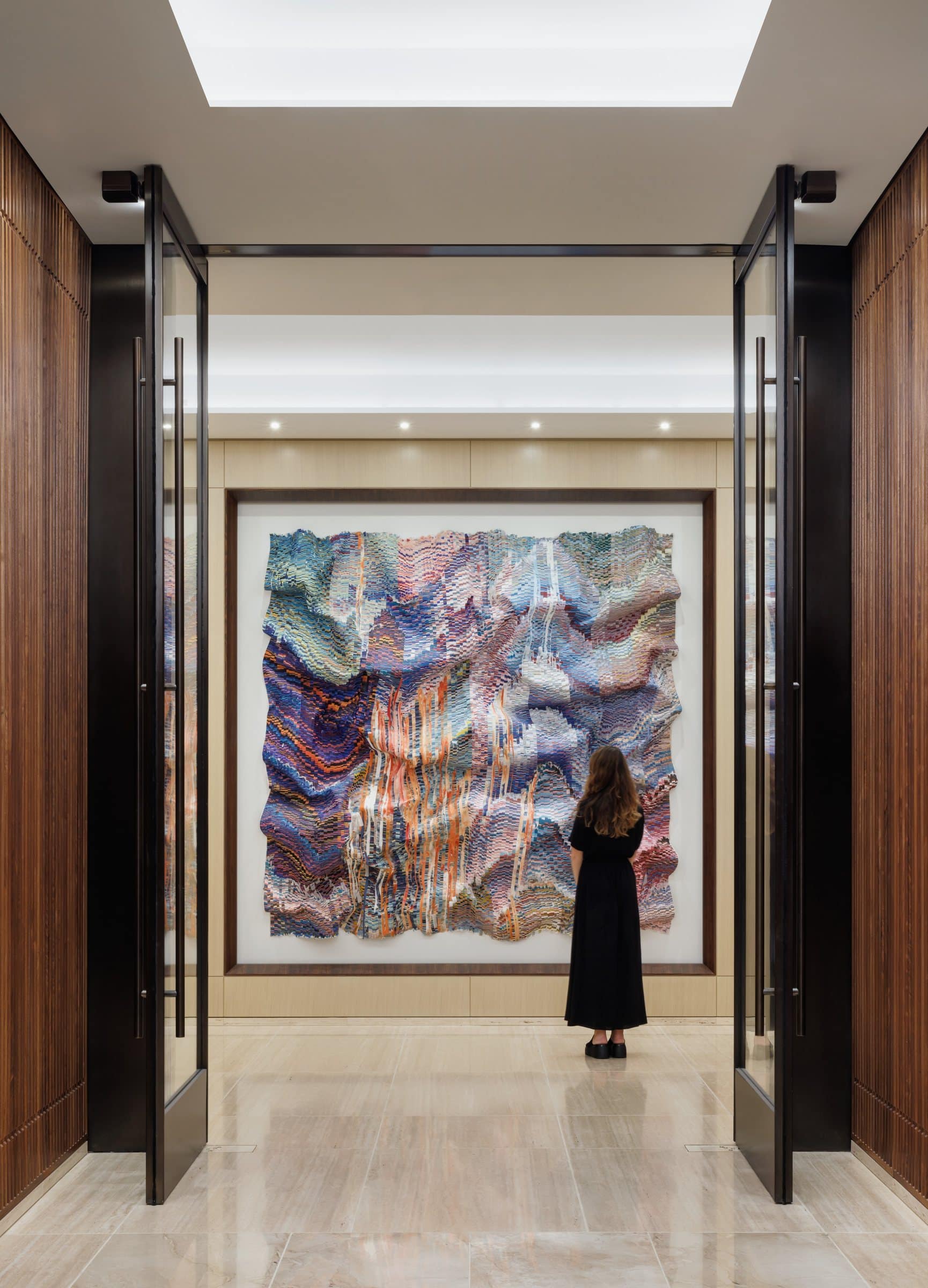 A visitor stands before the lavender and pink cut-silk work, seen through open glass doors