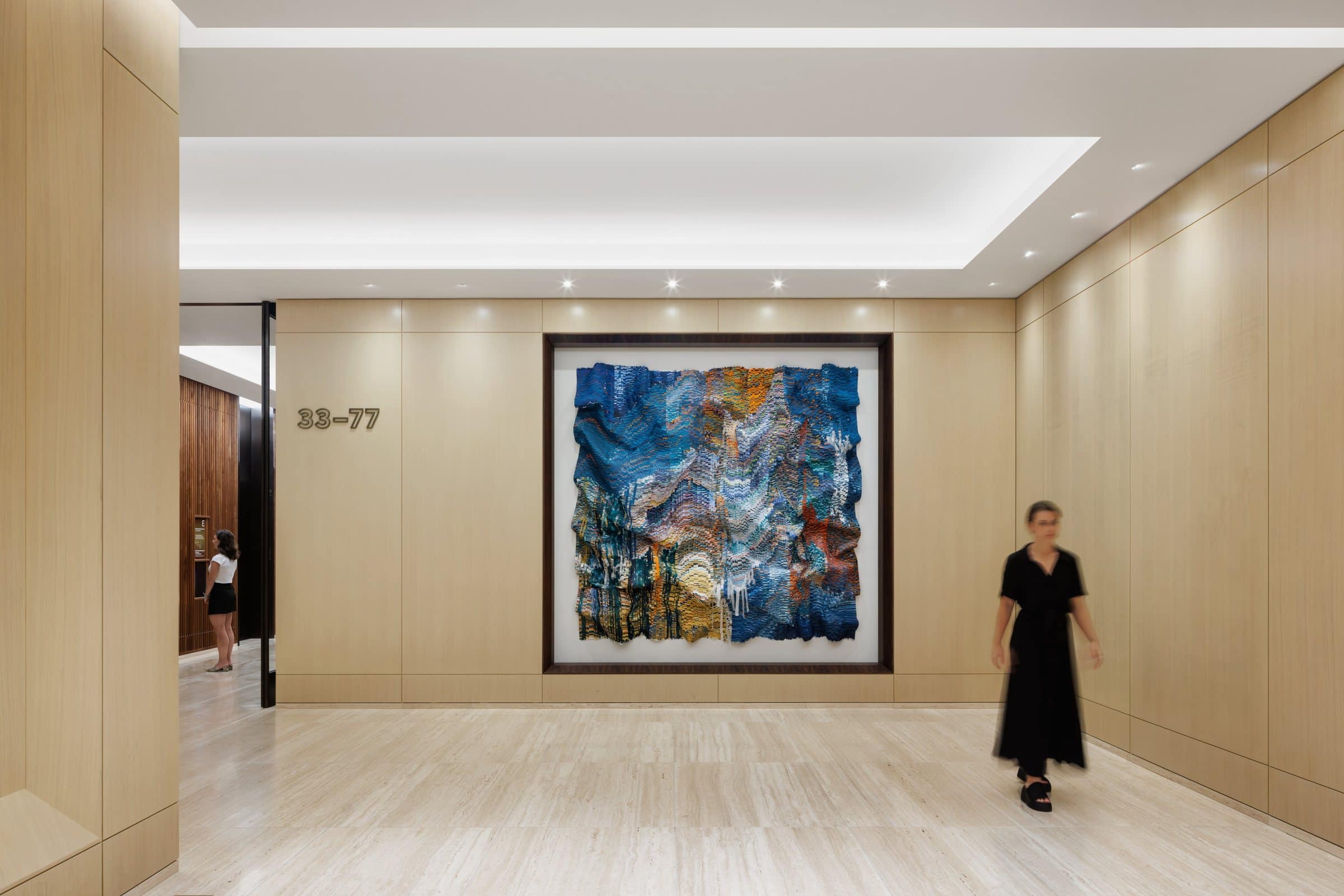 A visitor crosses the broad sky-lobby corridor in front of the blue-and-gold textile work