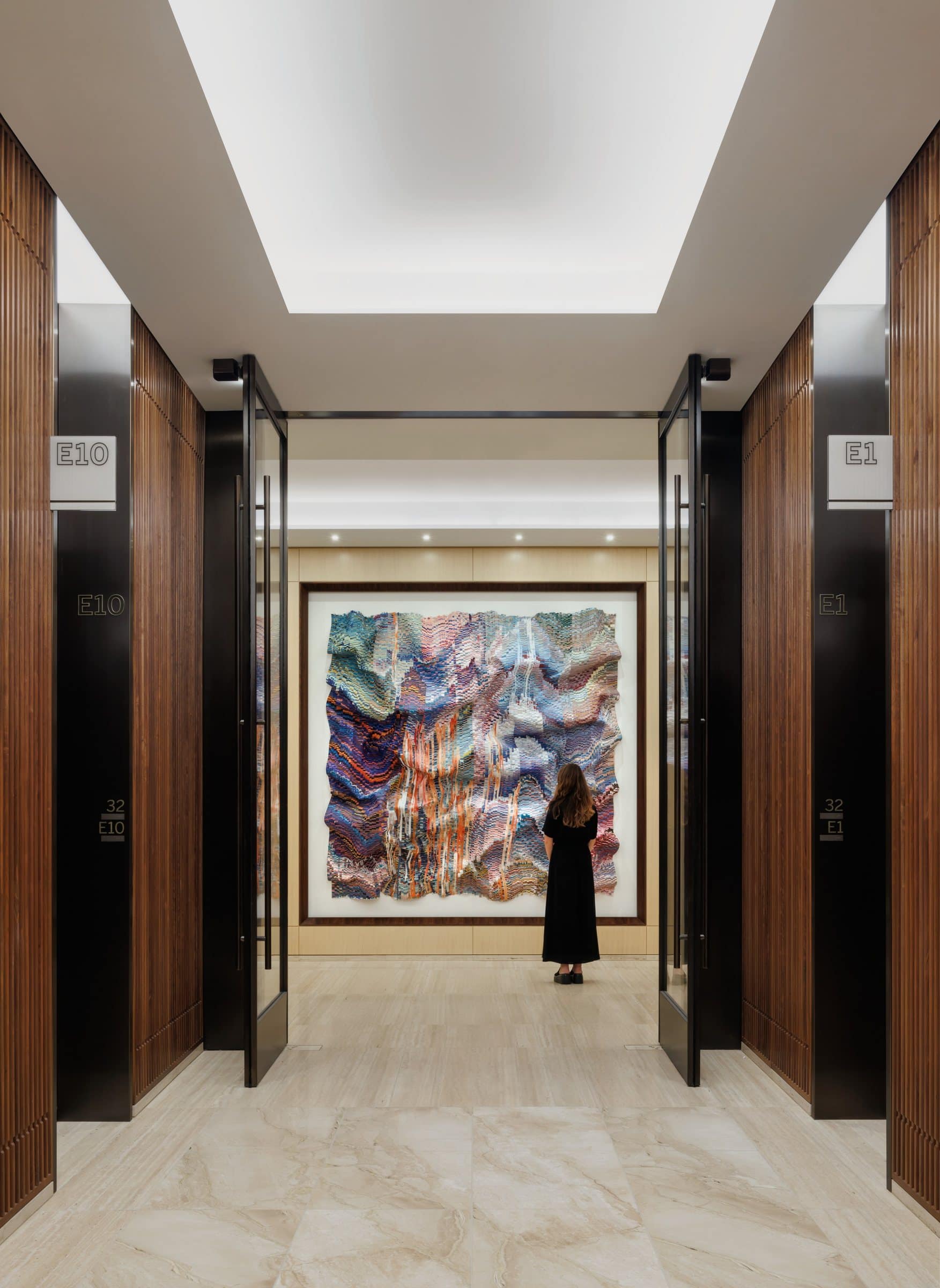 A visitor studies the lavender and pink textile work at the end of the elevator corridor