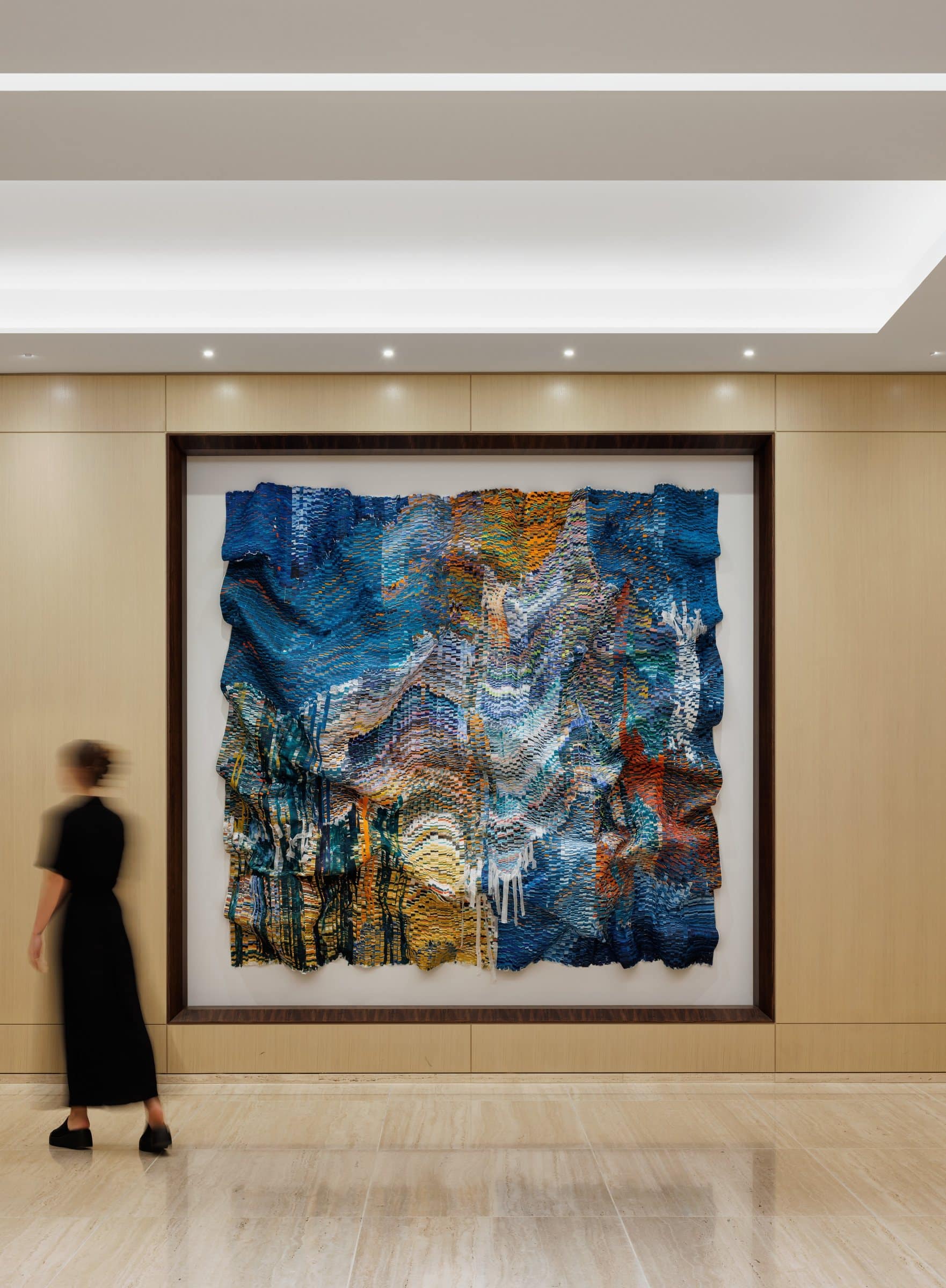 A visitor walks beside the blue-and-gold rippling silk work in its recessed wall frame
